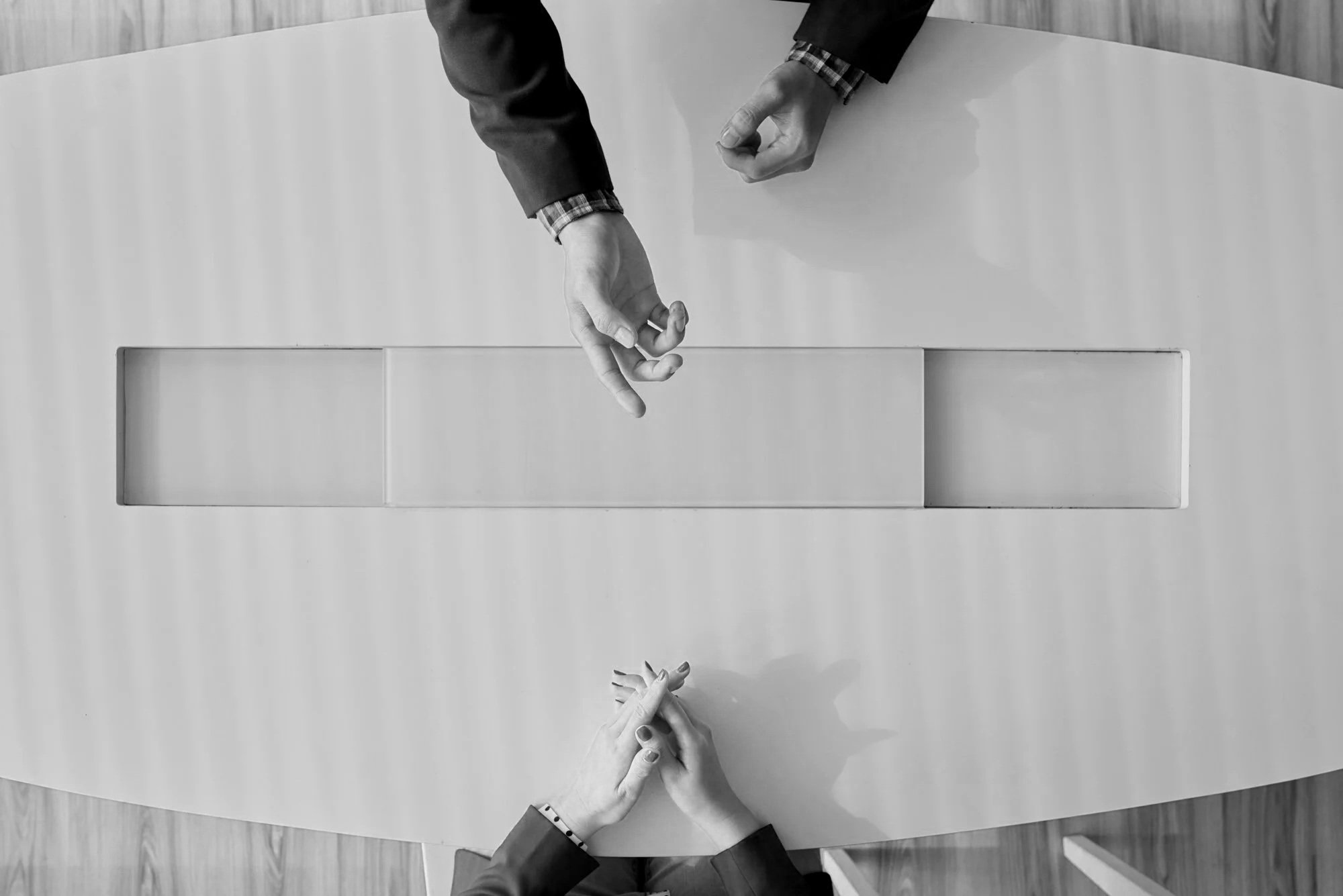 Business handshake at a meeting table with one person making a gesture and cut-out hand figures at the bottom.