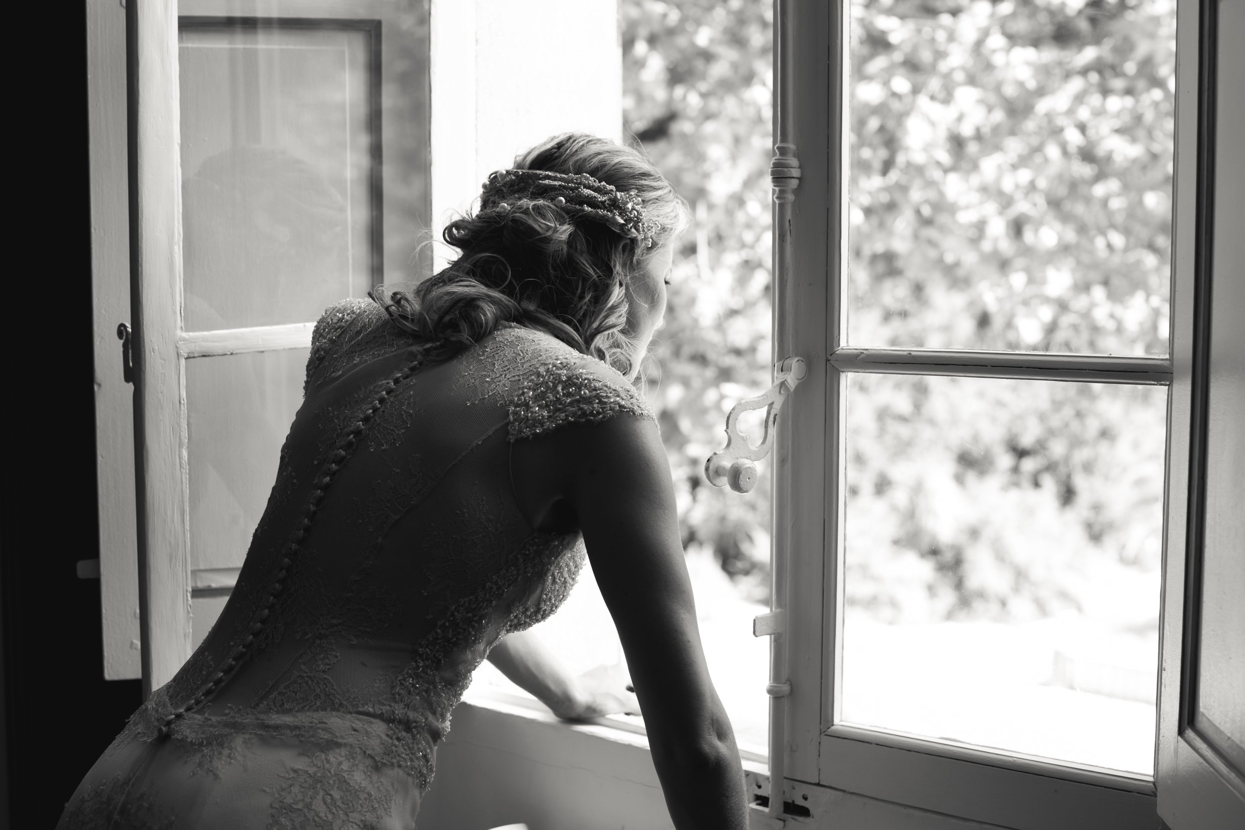 Een vrouw in een trouwjurk kijkt door een open raam, zwart-wit foto.