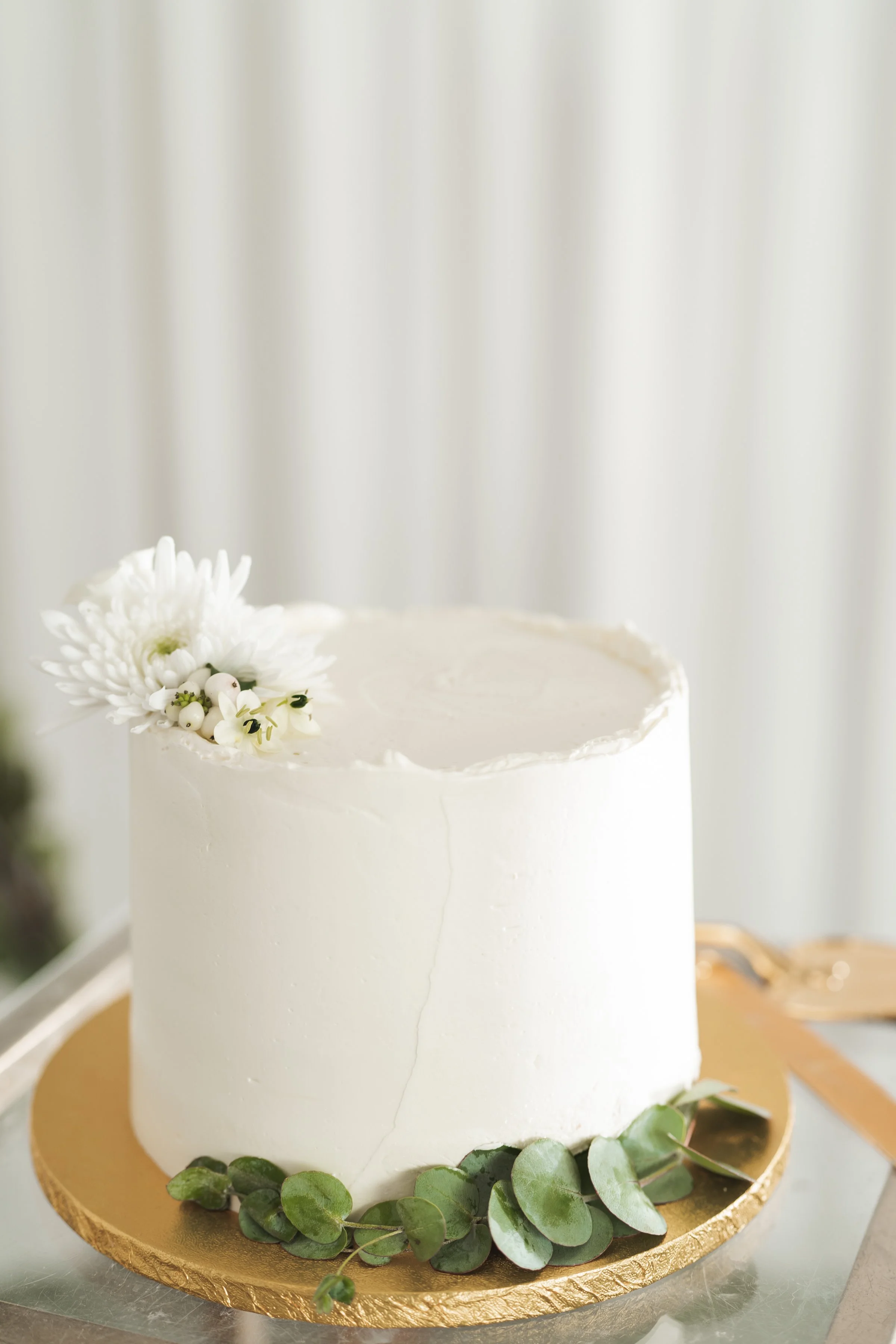 Wit vierlaagse taart met bloemen en bladeren, decoratief op een gouden bord.