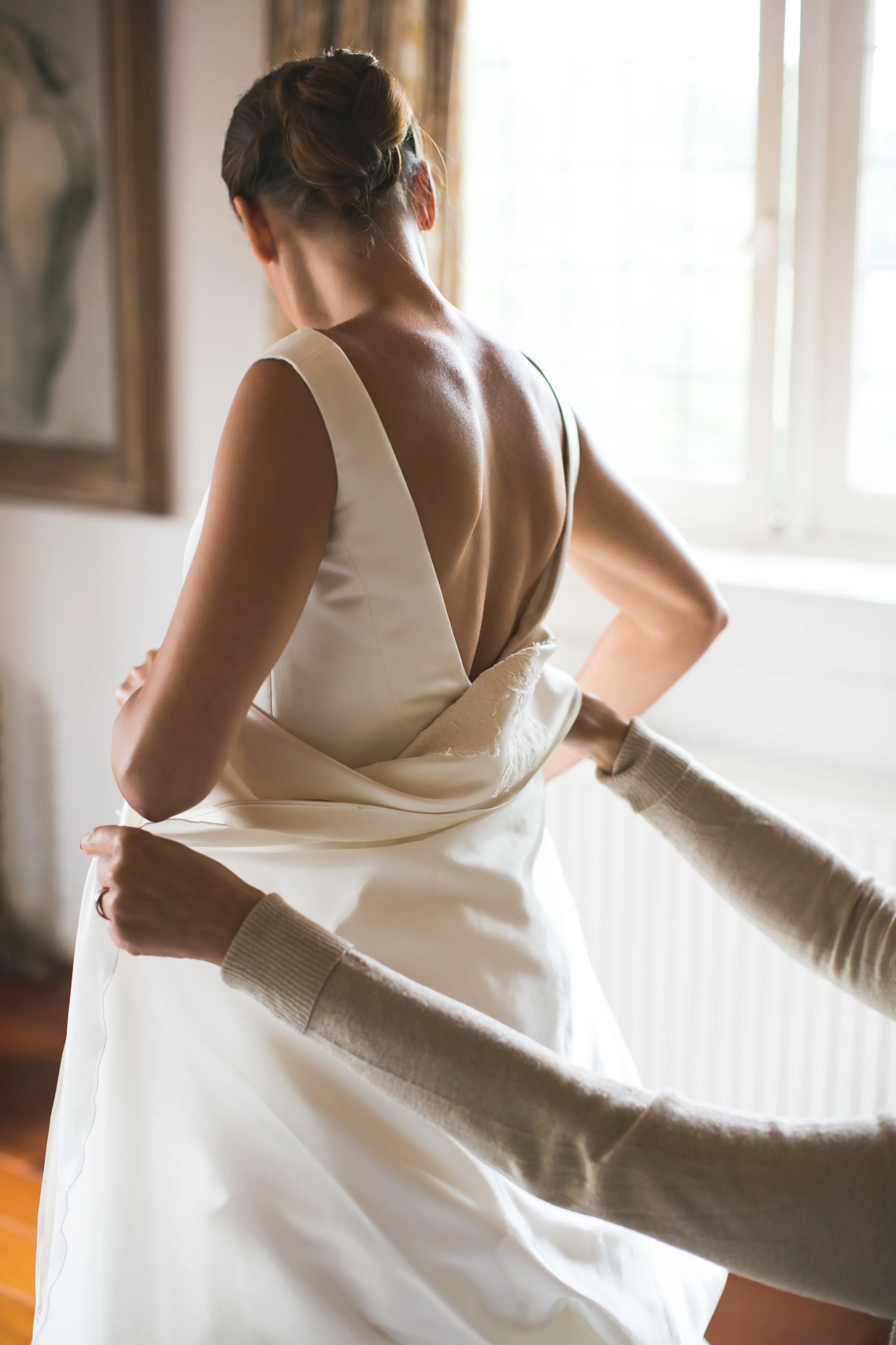 Vrouw in een witte jurk wordt geholpen met haar trouwjurk.