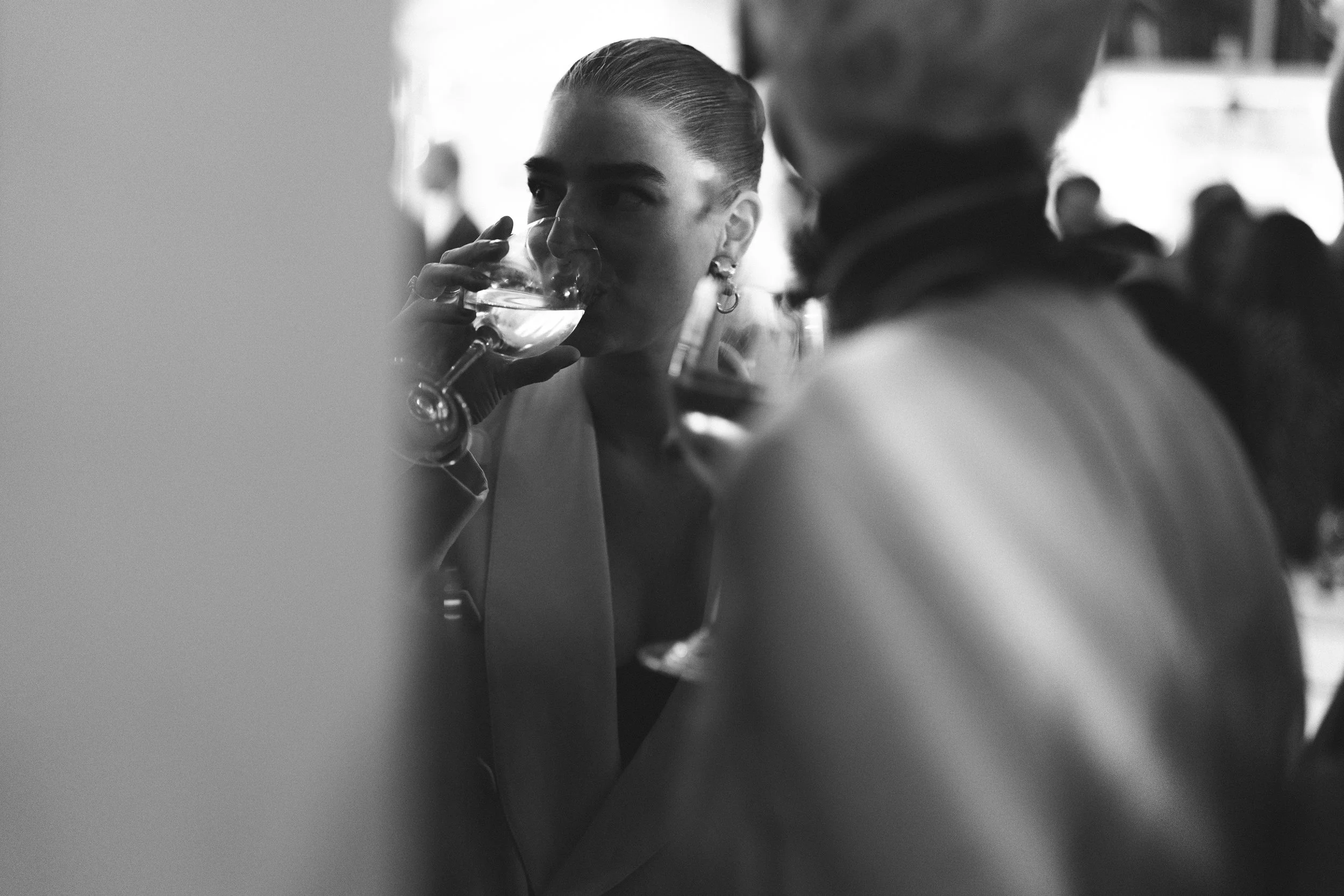 Een vrouw drinkt uit een glas wijn tijdens een sociale gelegenheid, omringd door andere mensen.