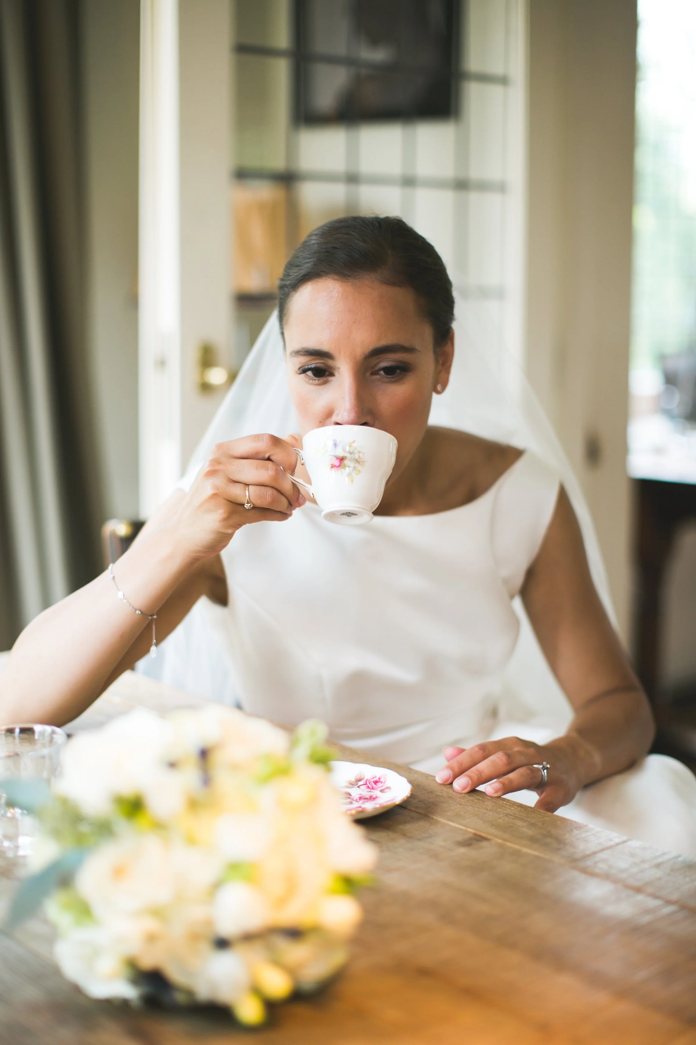 Vrouw in witte jurk met sluier drinkt thee uit een porseleinen kopje