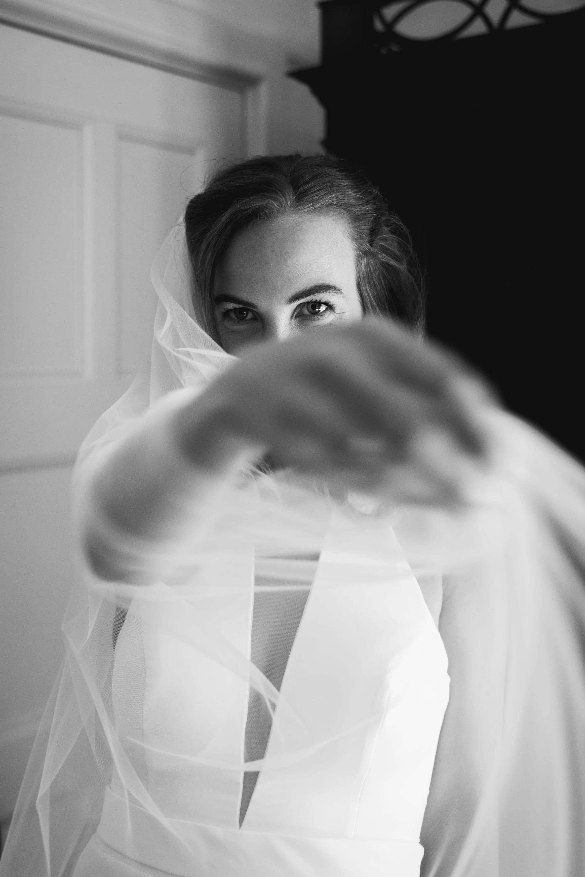Zwart-wit foto van een vrouw in een trouwjurk met een sluier die over haar gezicht hangt, haar hand uitgestoken naar de camera.