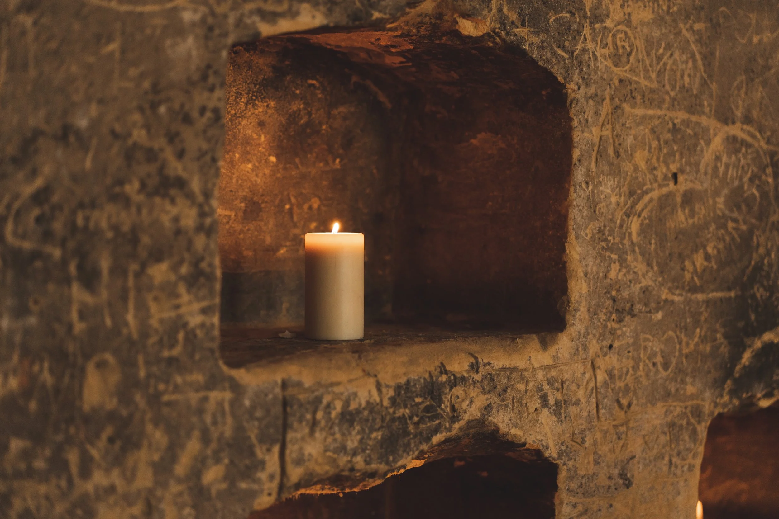 Een brandende witte kaars geplaatst in een stenen nisje in een oude muur met graffiti.