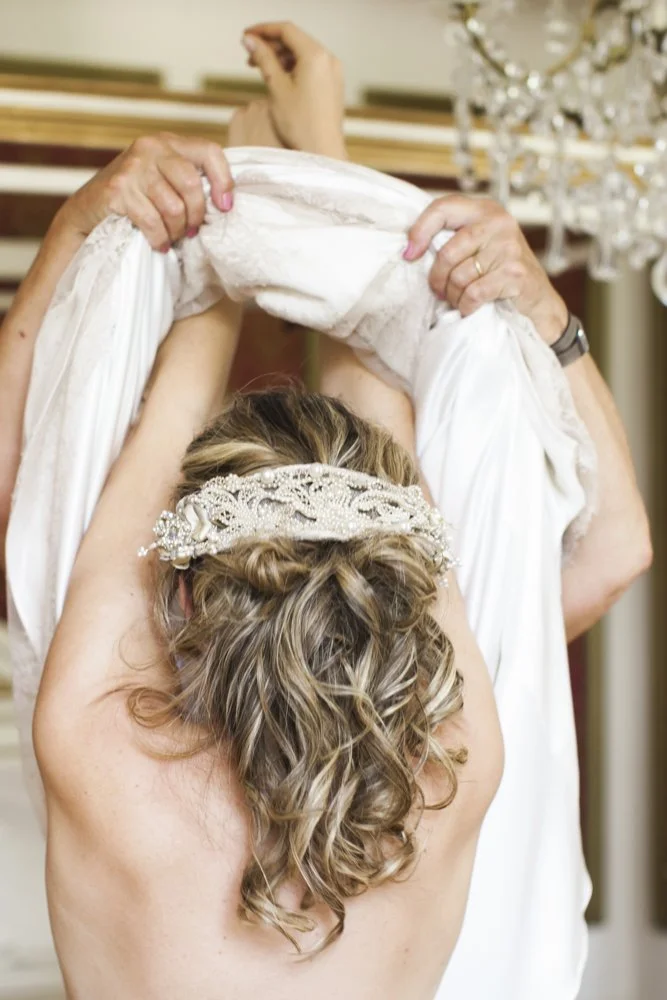 Een vrouw met een haarband met parels en kralen kamt haar trouwjurk.