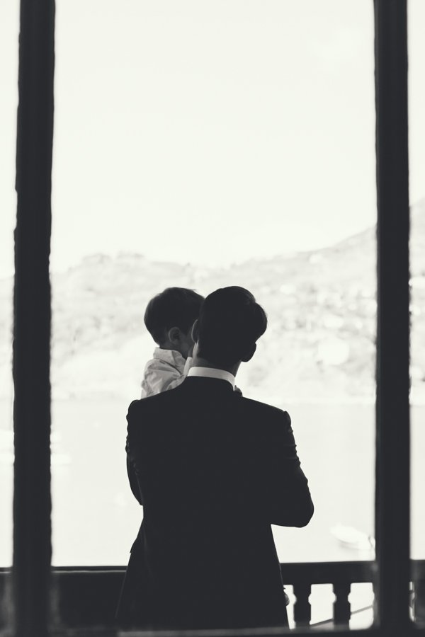 Silhouet van een man in een pak die een kind vasthoudt bij een groot raam, met een uitzicht op een berglandschap op de achtergrond.