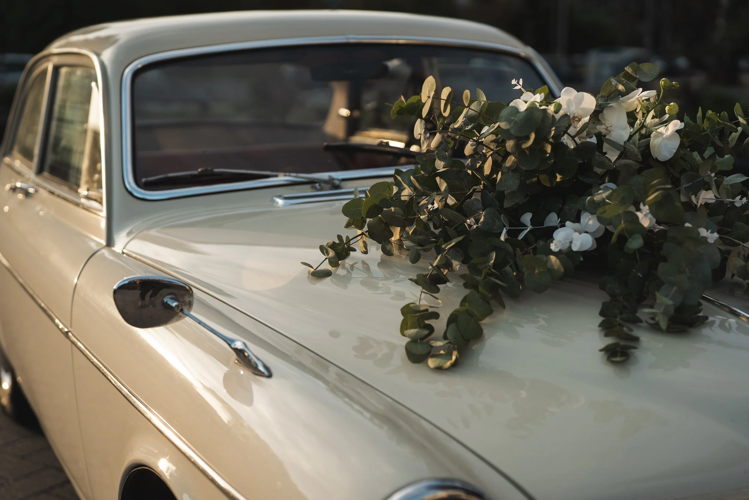 Een klassieke witte auto met een bloemenarrangement op de motorkap, gefotografeerd tijdens de schemering.