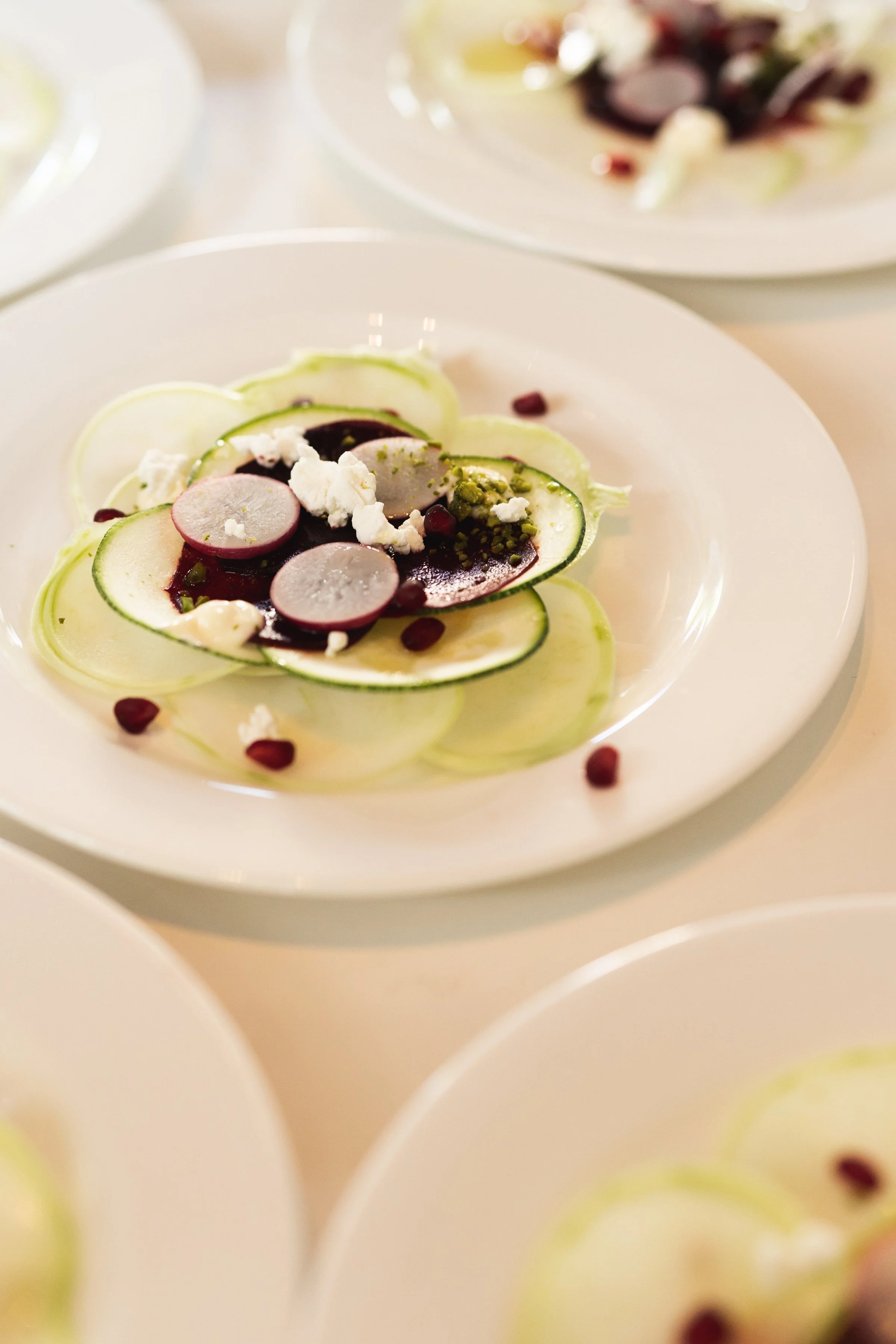 Salade met dunne plakjes komkommer, radijs en blauwe bes, afgewerkt met witte kaas en peterselie, geserveerd op een wit bord.