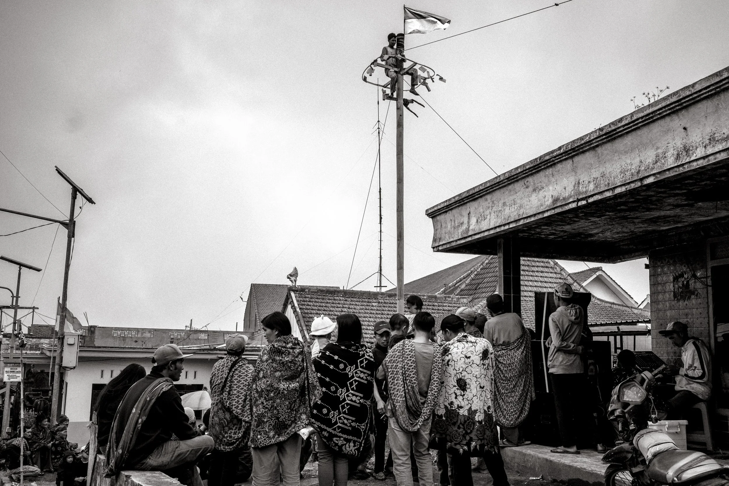 Villagers gather below as a competitor reaches the top of the greased pole
