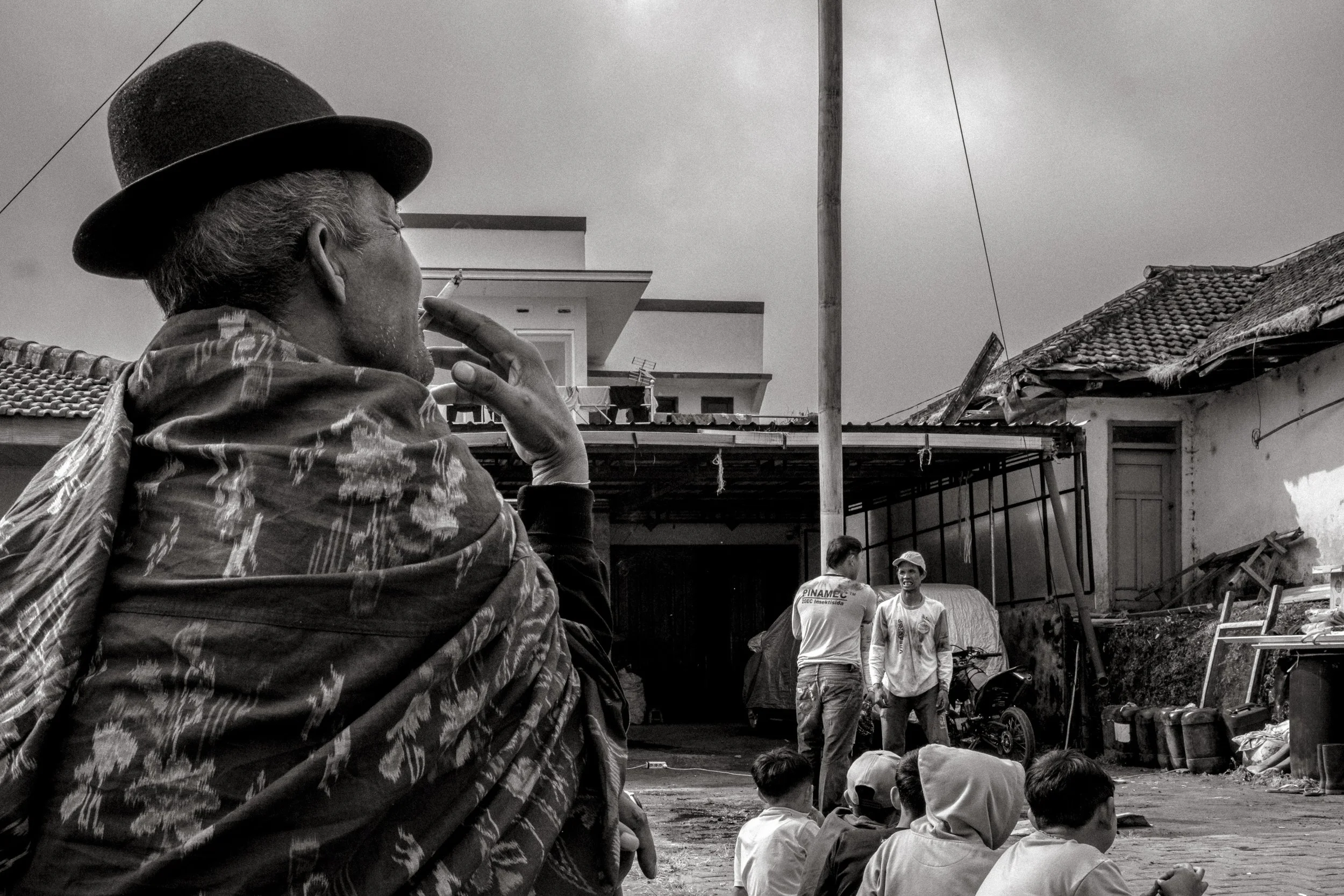 A spectator watches as climbers prepare to begin, a patterned cloth draped over his shoulders. Ngadas is one of the highest villages in Java at 2,150m, with temperatures dropping to as low as 8°C in August. Ngadas, East Java, Indonesia. 21 August 202