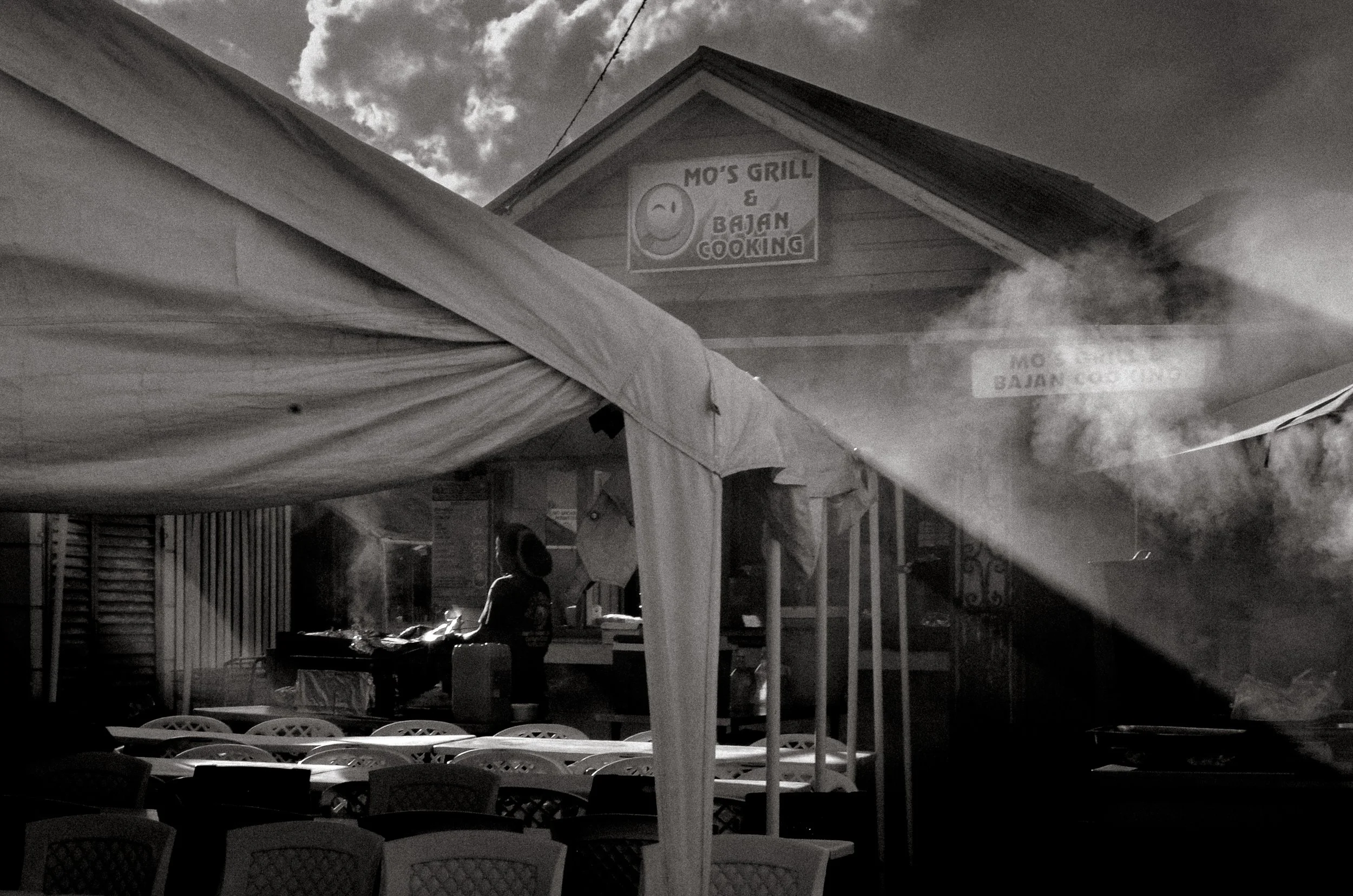 Smoke rises as stalls prepare for the night before crowds arrive. Oistins, Barbados. December 2022.