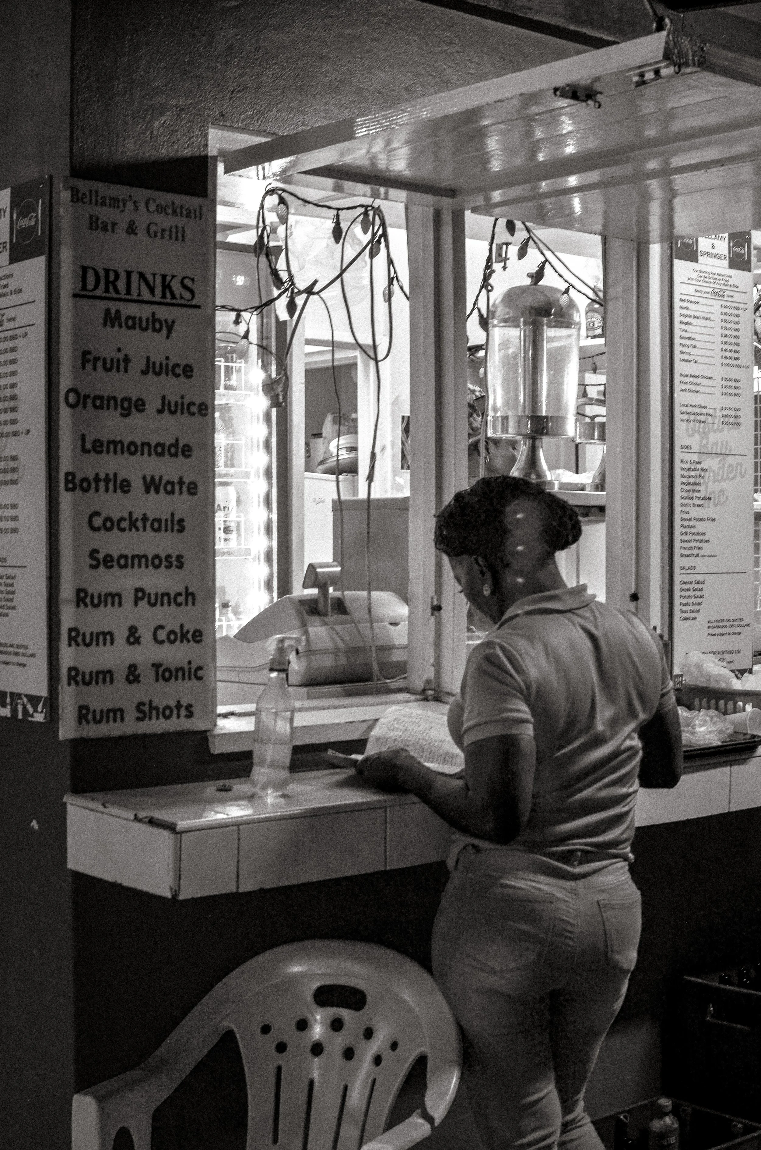 A waitress pauses at a drinks stall. Oistins, Barbados. December 2022.