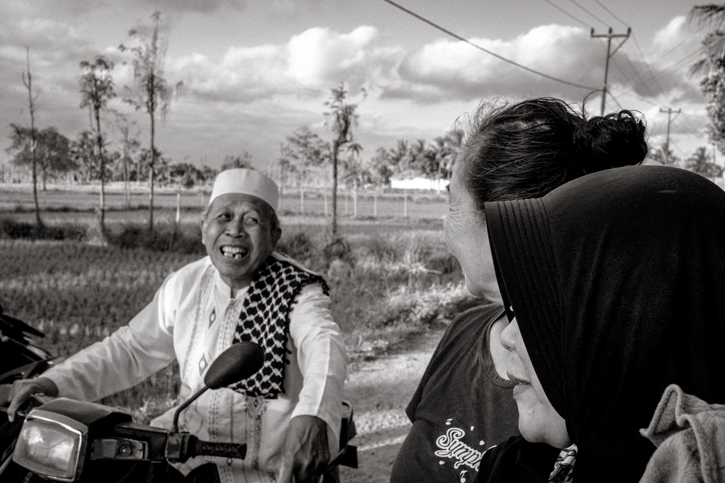 A man on a motorbike smiles toward the crowd as women watch from the roadside