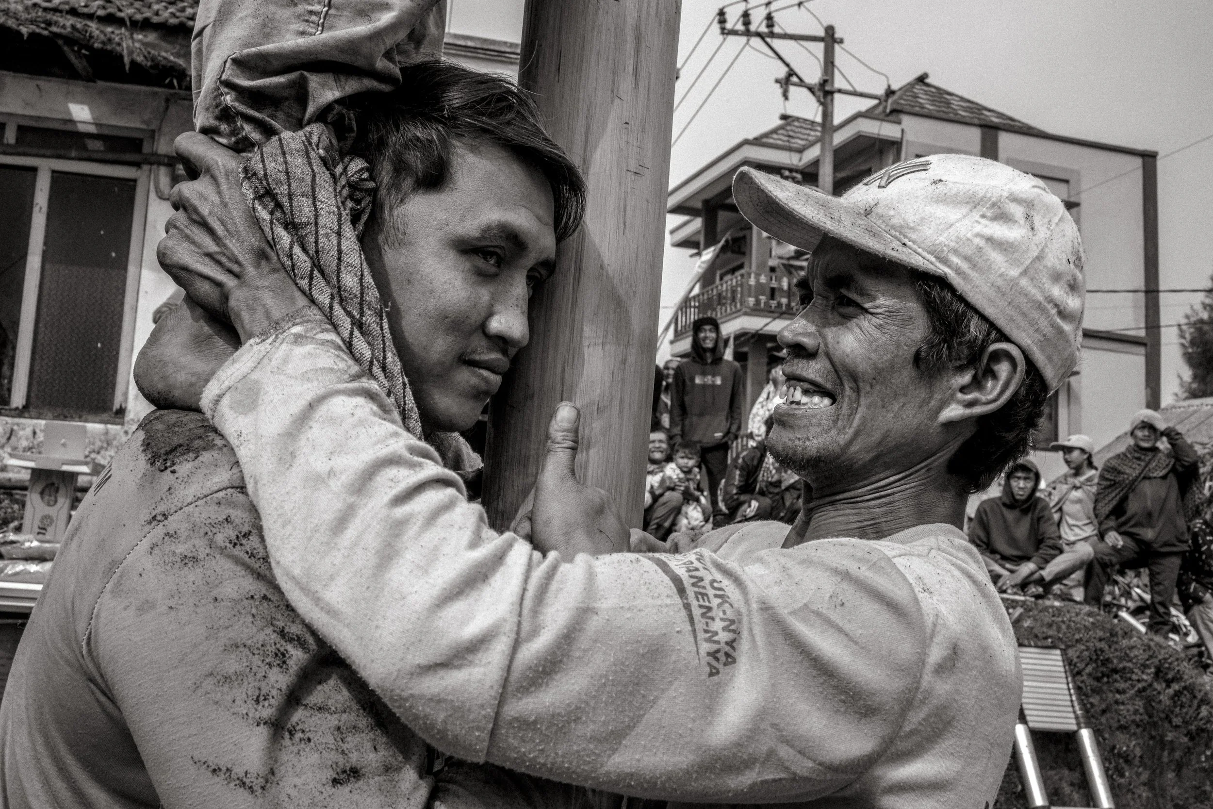 Two competitors brace the pole and support the base as teammates climb above them