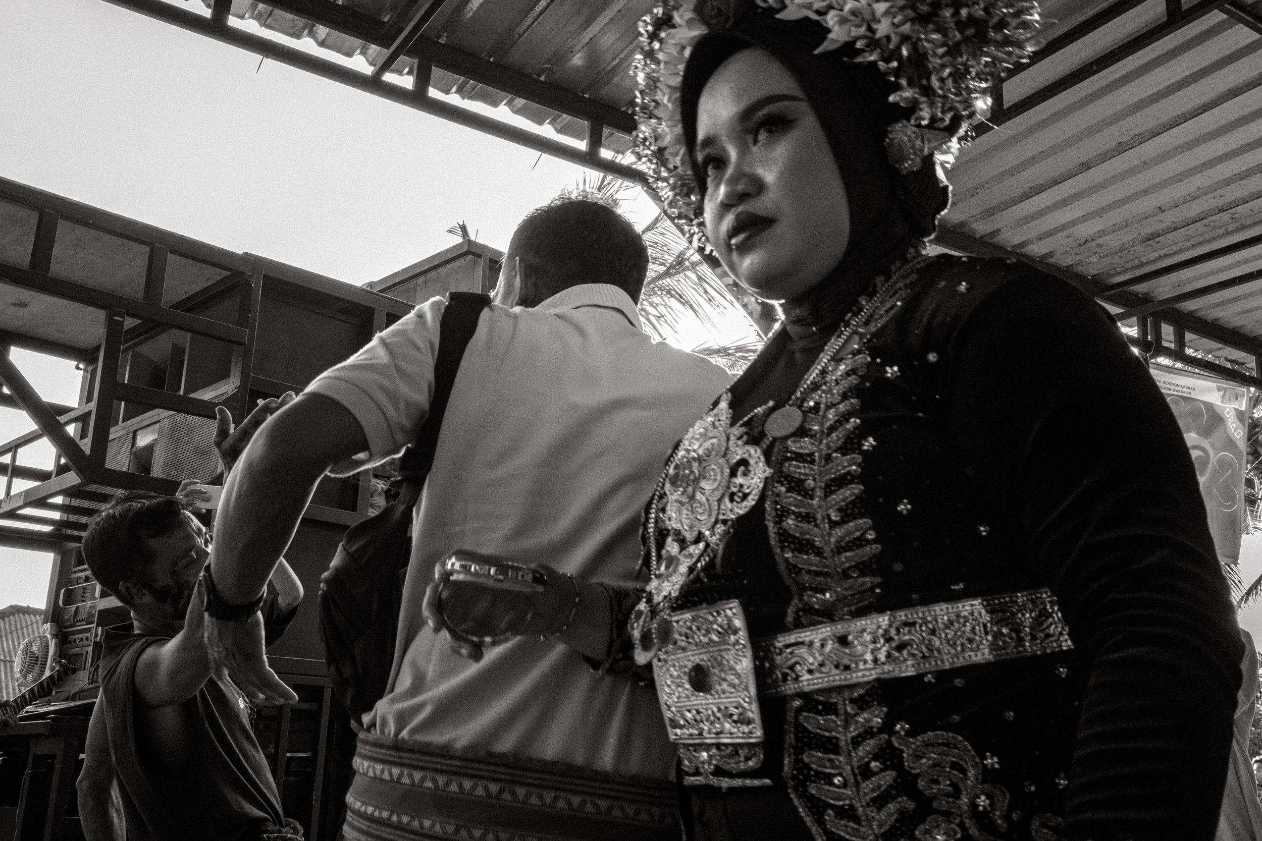 The bride stands at the edge of the dance holding a small case as people move past