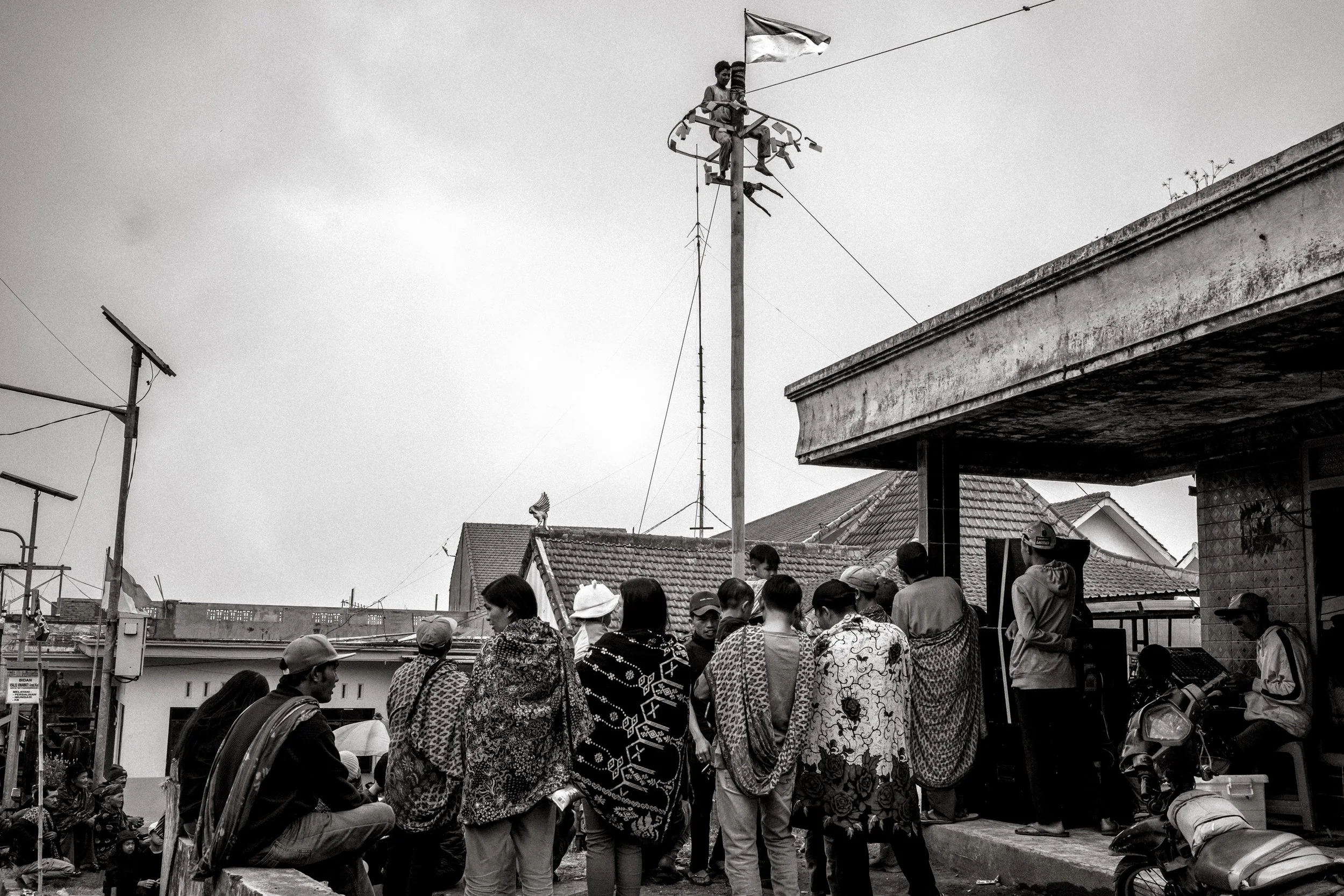 A competitor reaches the top of the greased pole beside the Indonesian flag, as spectators watch from the side. Ngadas, East Java, Indonesia. 21 August 2025.