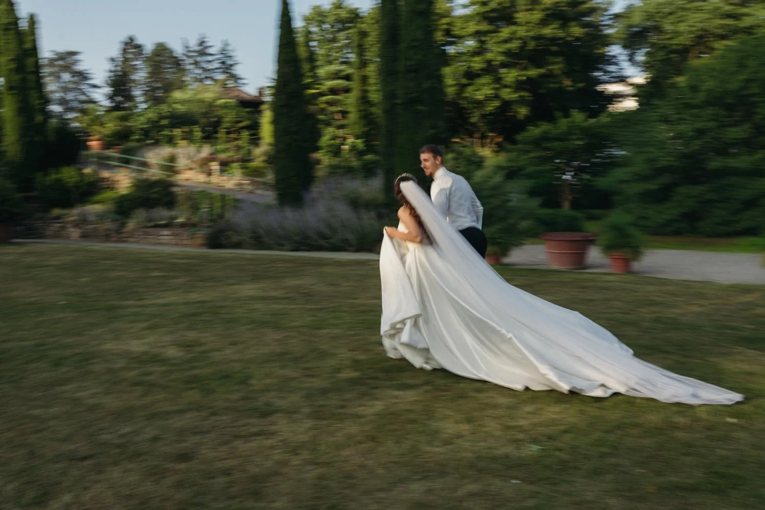Brautpaar läuft mit langem Schleier über die Wiese im Blühenden Barock Ludwigsburg während eines Hochzeitsporträts im Grünen