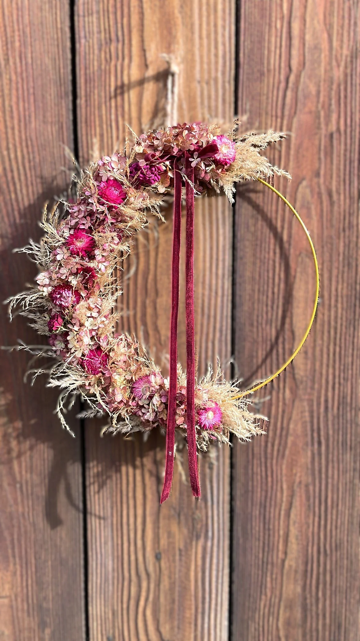 Hochzeitsmondkranz aus getrockneten Blumen in Pink und Beige, mit gelbem Rahmen, an einer Holztafel aufgehängt.