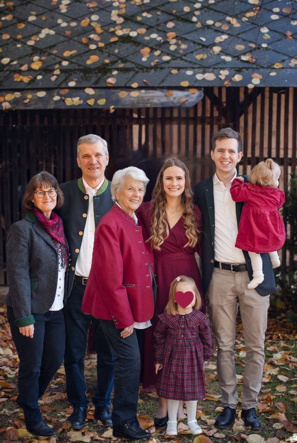 Mehrgenerationenfamilie im Freien mit Herbstlaub vor einem Holzgebäude.