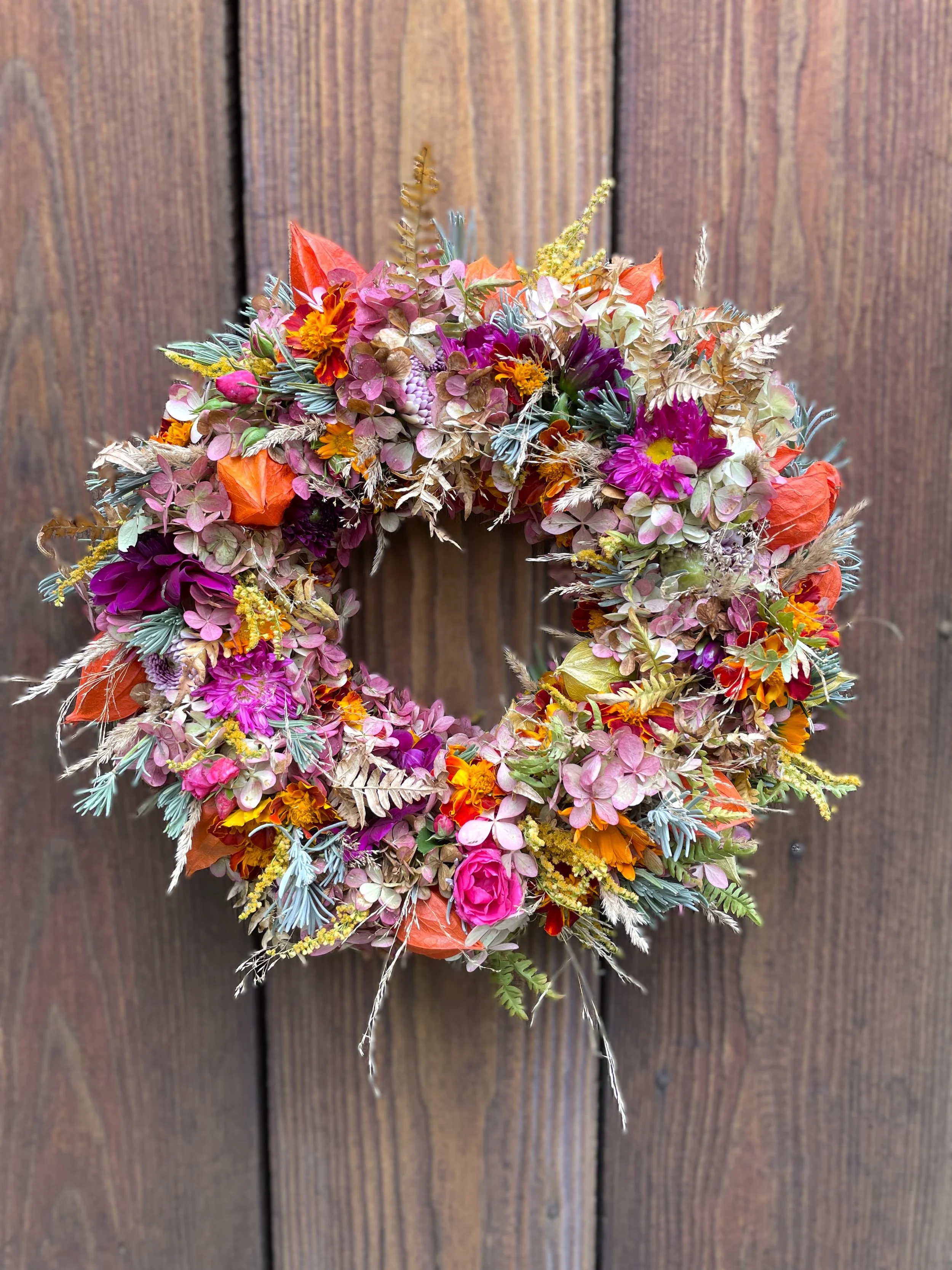 Bunter Herbstlichter Kranz aus Blumen und Blättern an einer Holztür.