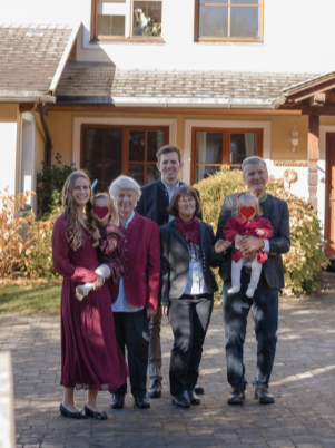 Fünf Familienmitglieder stehen nebeneinander vor einem Haus, einige halten Haustiere, alle lächeln in die Kamera.