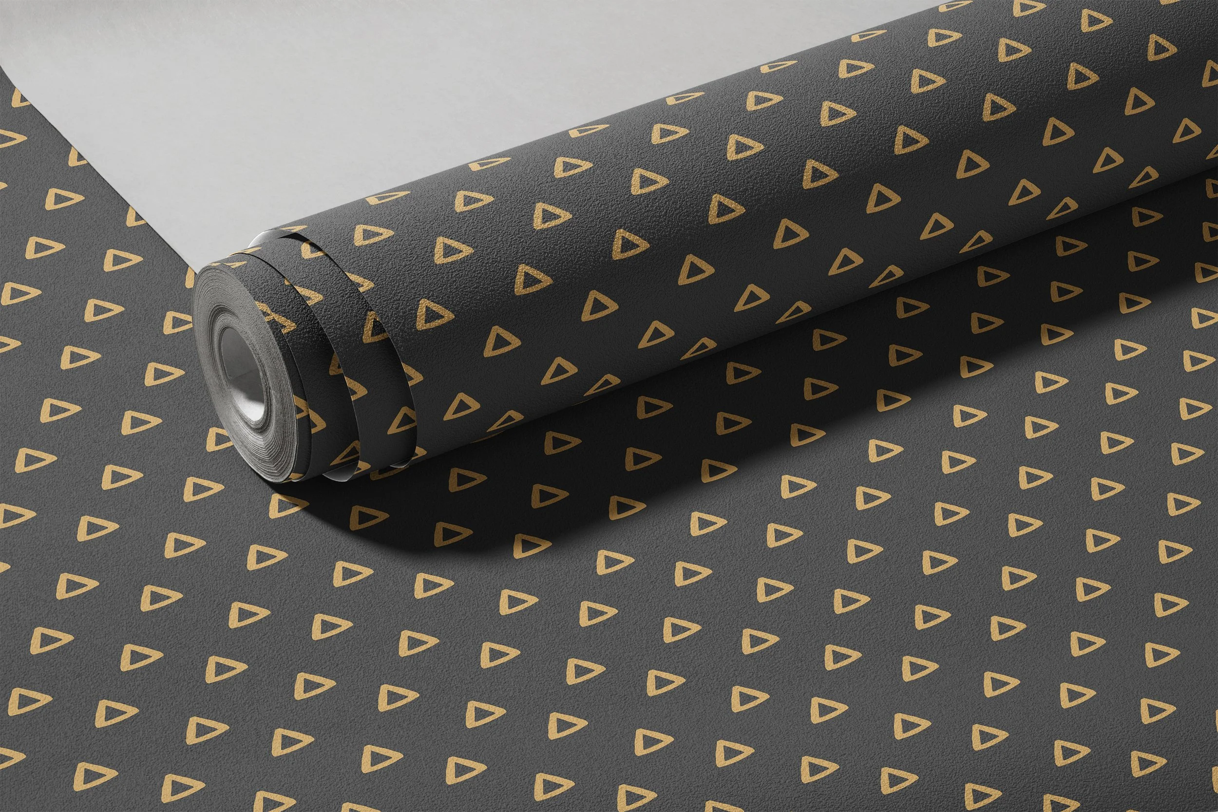 Rolled black wrapping paper with a pattern of gold triangles, partially unrolled to reveal a plain white sheet underneath.