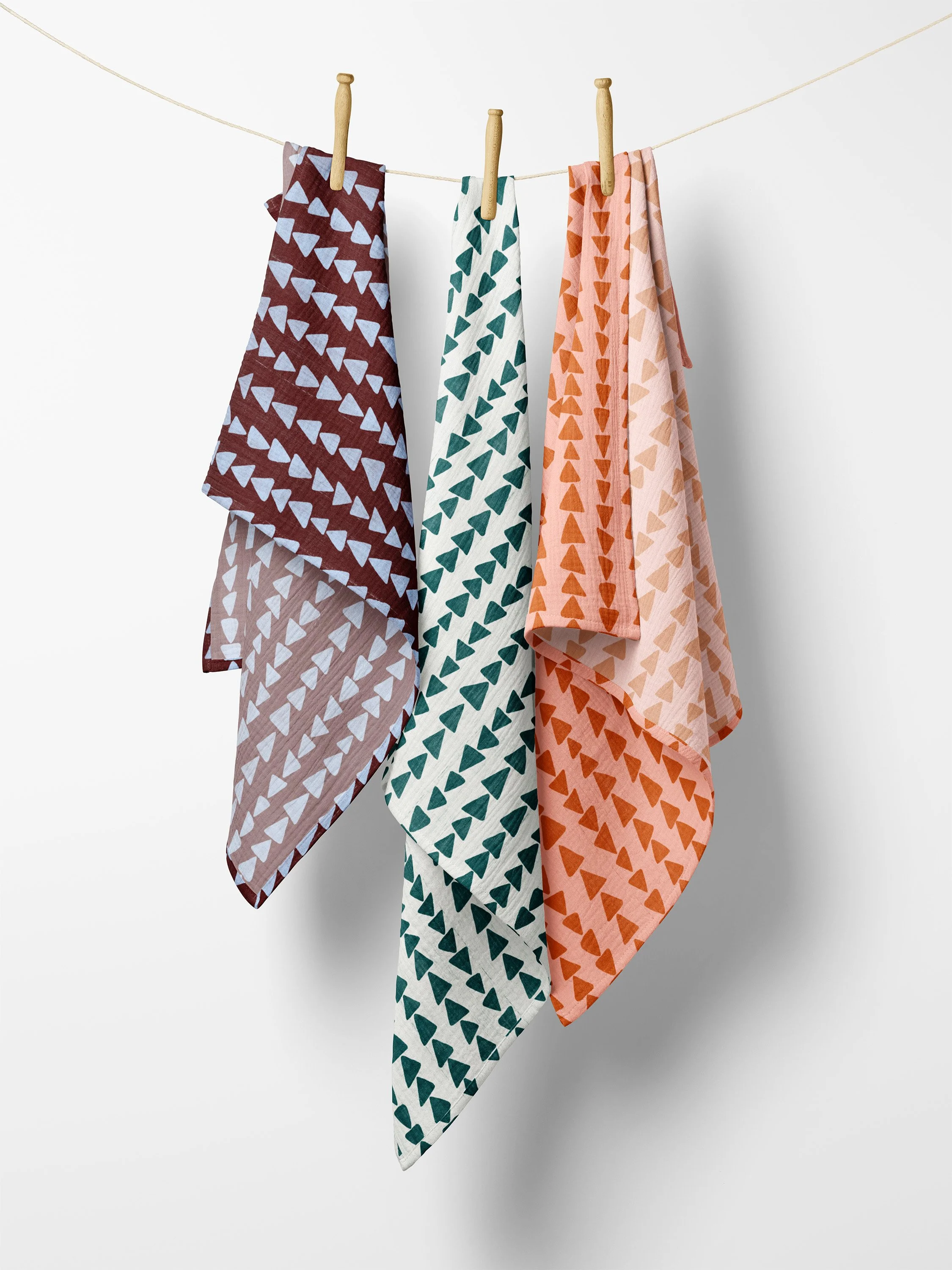 Three colorful bandanas with geometric triangle patterns hanging on a clothesline against a plain white background.