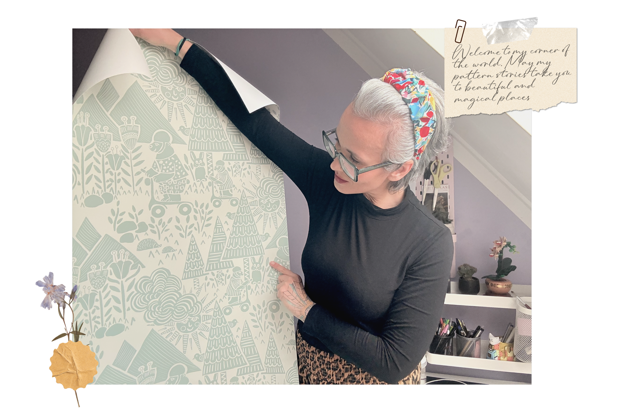 Woman with glasses and colorful headband pointing at a large piece of art in a room decorated with plants and art supplies, with a note that reads, 'Welcome to my corner of the world. May my pattern stories take you to beautiful and magical places.'