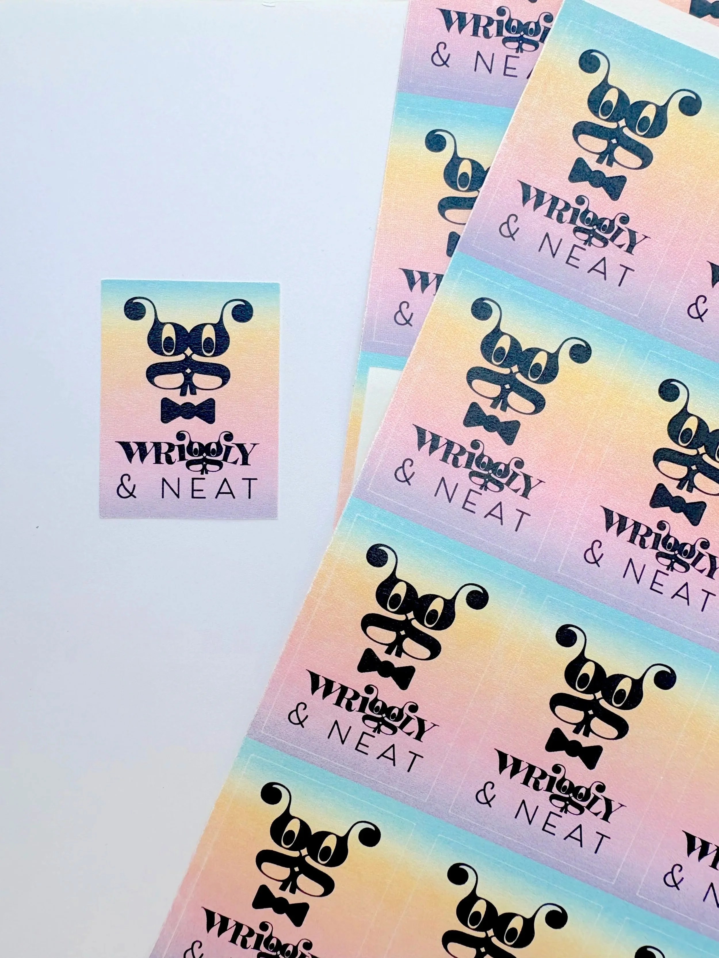 Colorful tickets with a pastel rainbow background and the text 'Wrigly & Neat' along with a stylized skull and bowtie logo.