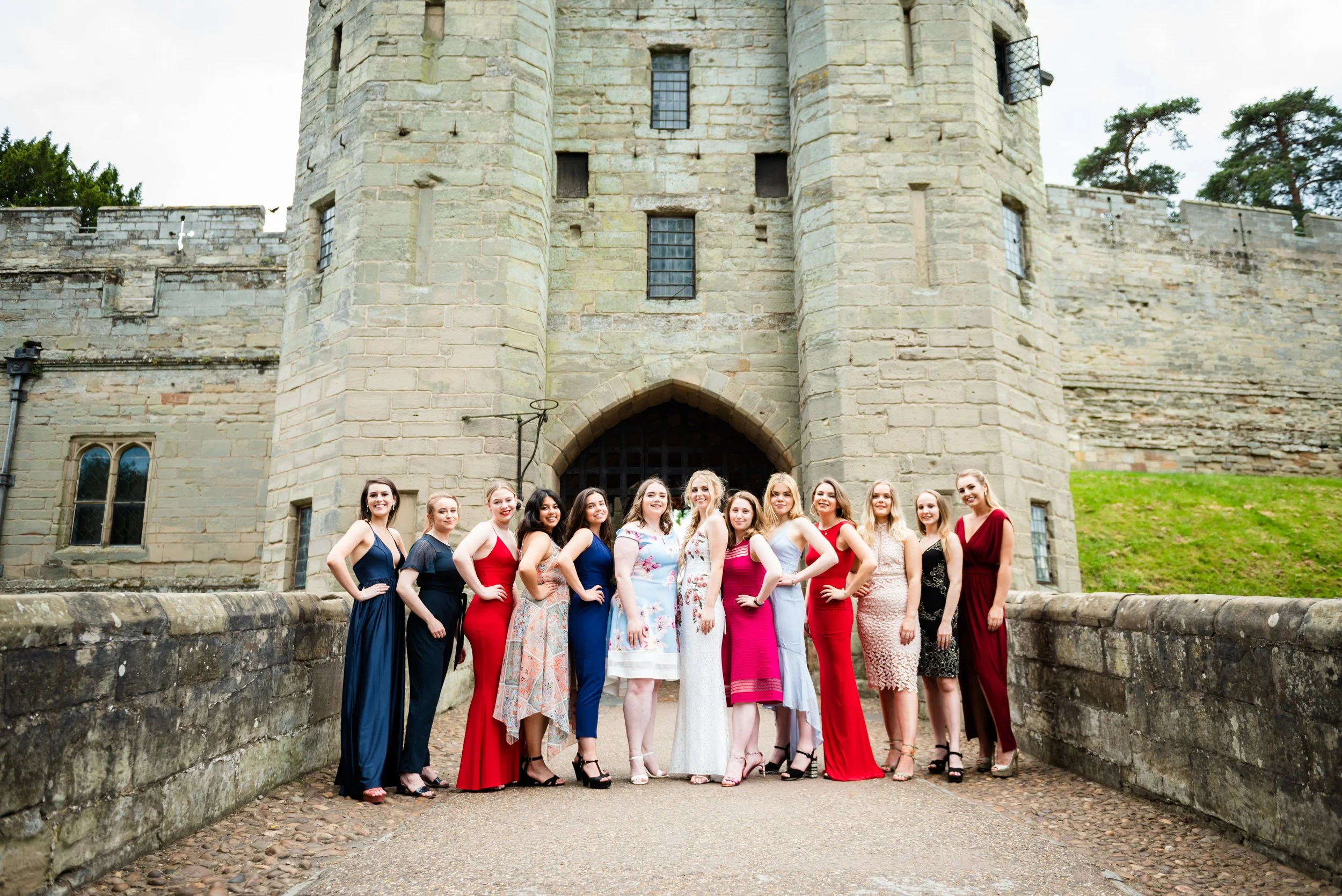 Group shot of women dressed in colorful evening gowns standing in front of historic Warwick Castle for a birthday party