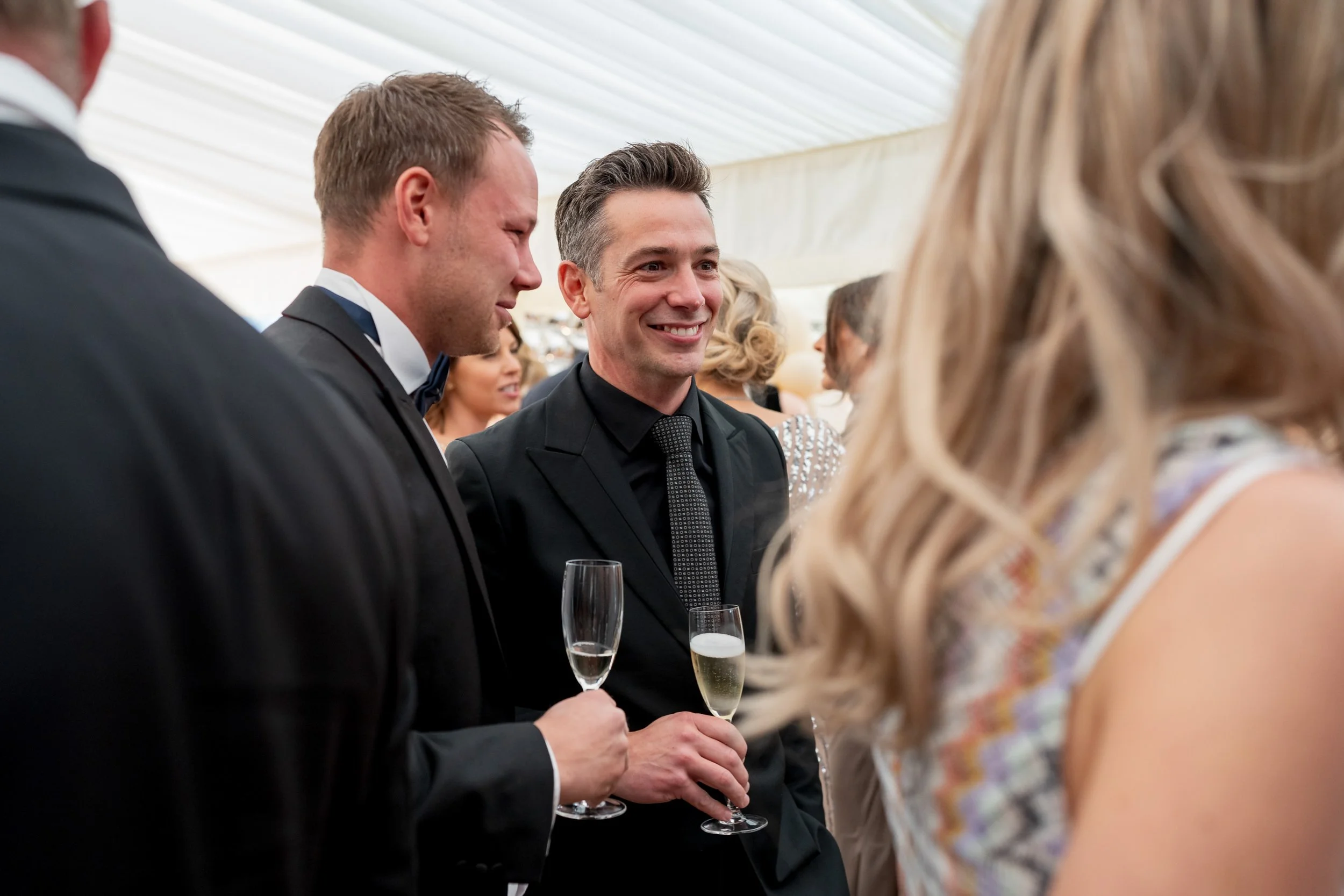 People dressed in formal attire at a reception event, holding glasses of champagne and socializing.