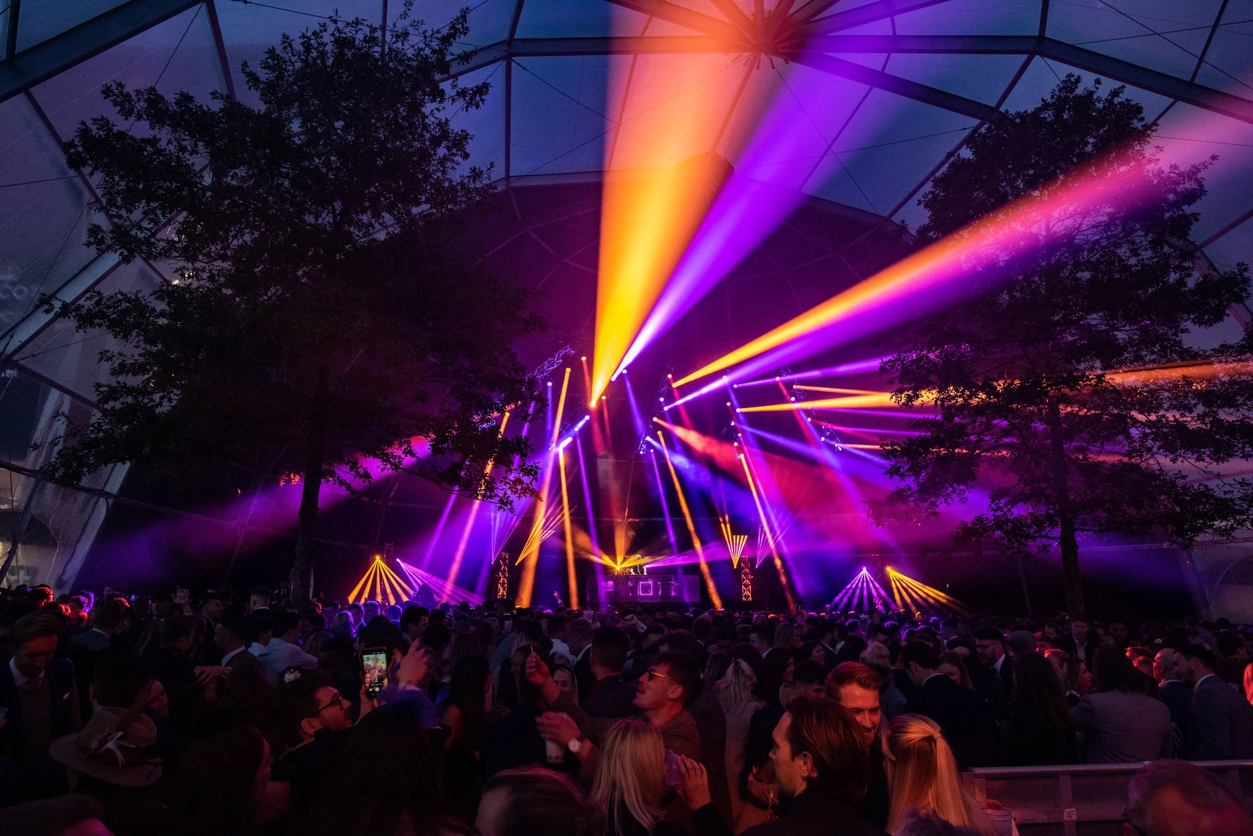 After party event concert  at Royal Ascot with a large crowd, colorful stage lighting, and trees inside the Igloo structure from Fews Marquees.