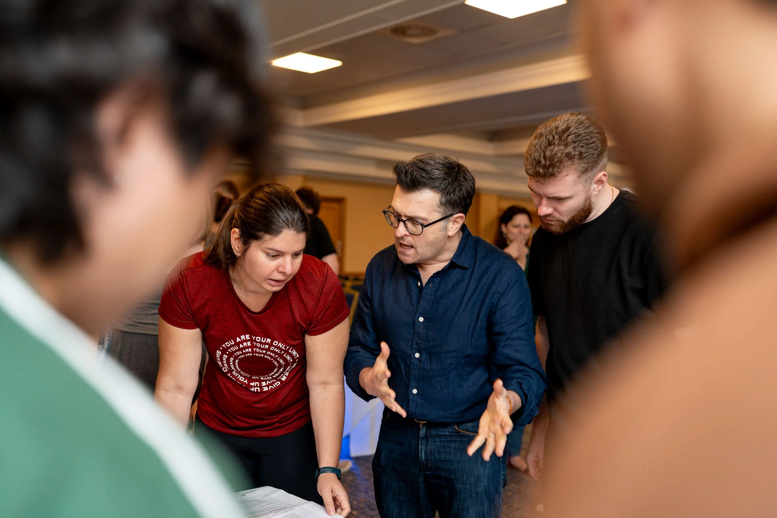Group of people engaged in a discussion activity at a work conference, focusing on a man in glasses speaking and two women listening intently.
