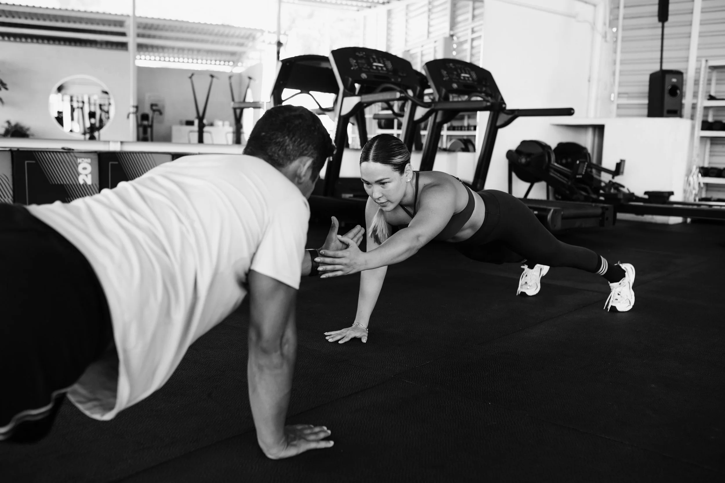 Eine junge Frau macht Liegestützen in einem Fitnessstudio während ein Trainer sie korrigiert.