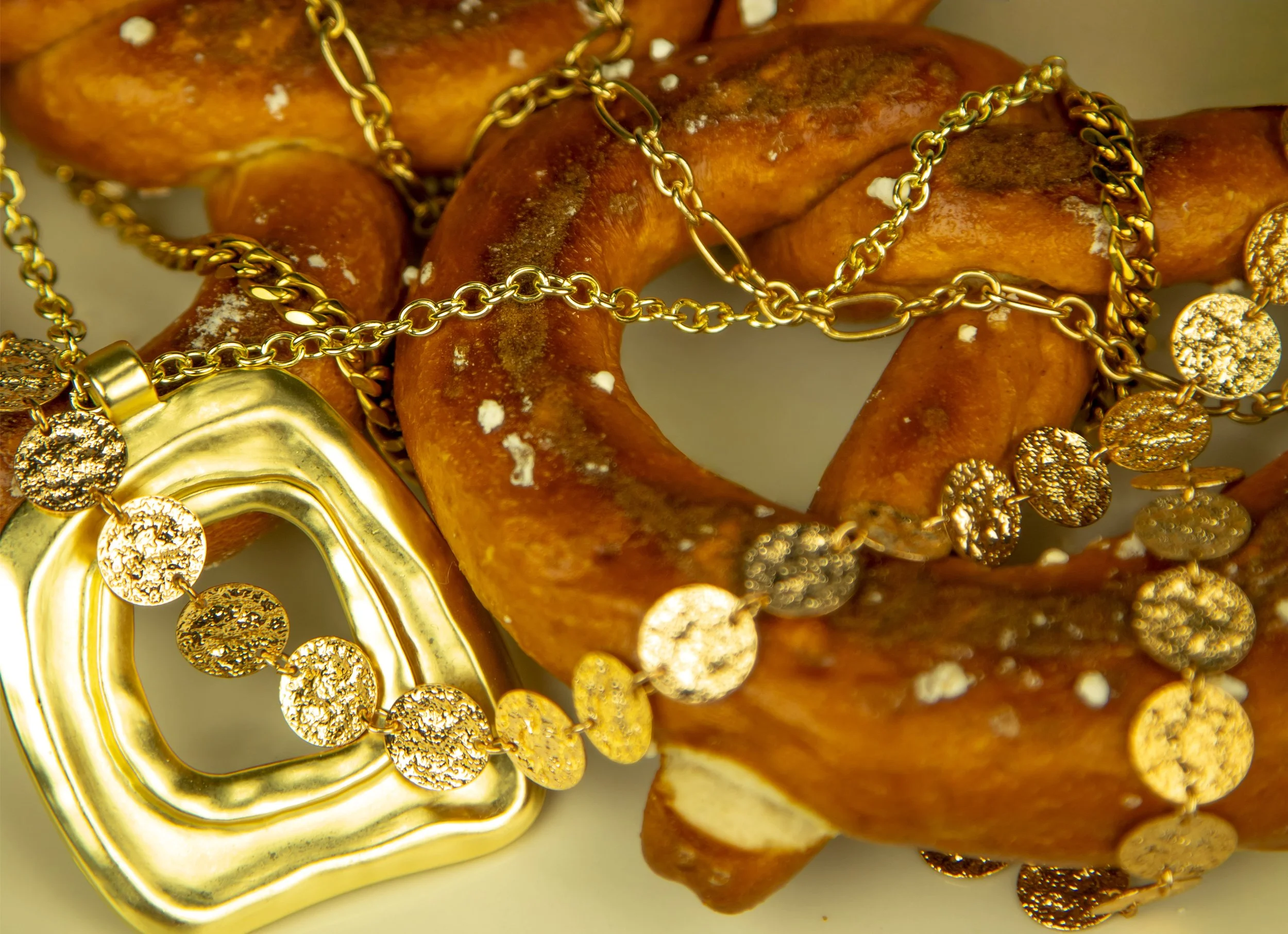 Gold jewelry with circular pendants draped over a bagel with white sprinkles.