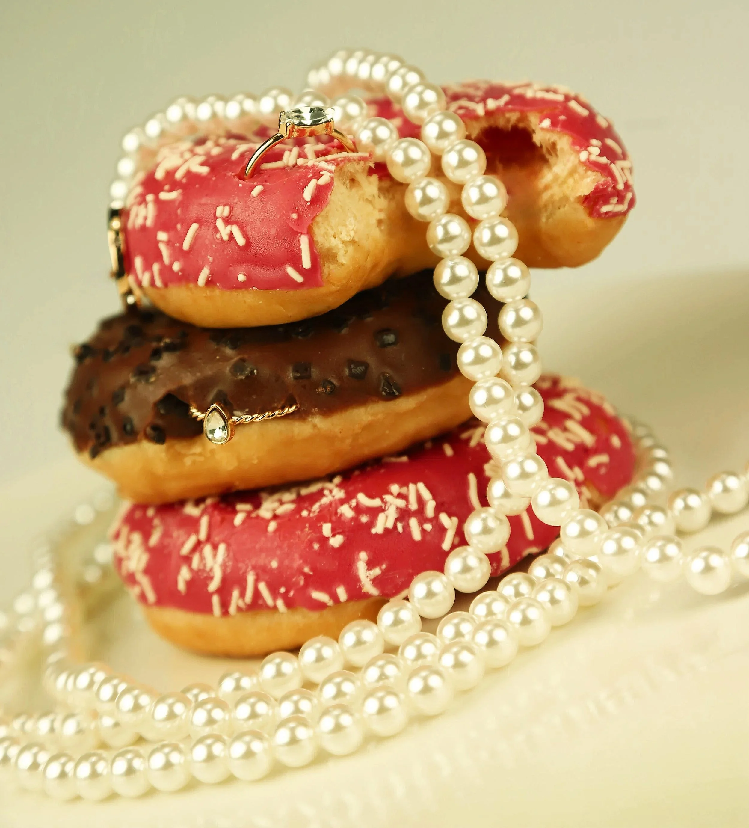 Stack of three decorated donuts with pearl necklaces and rings on top.