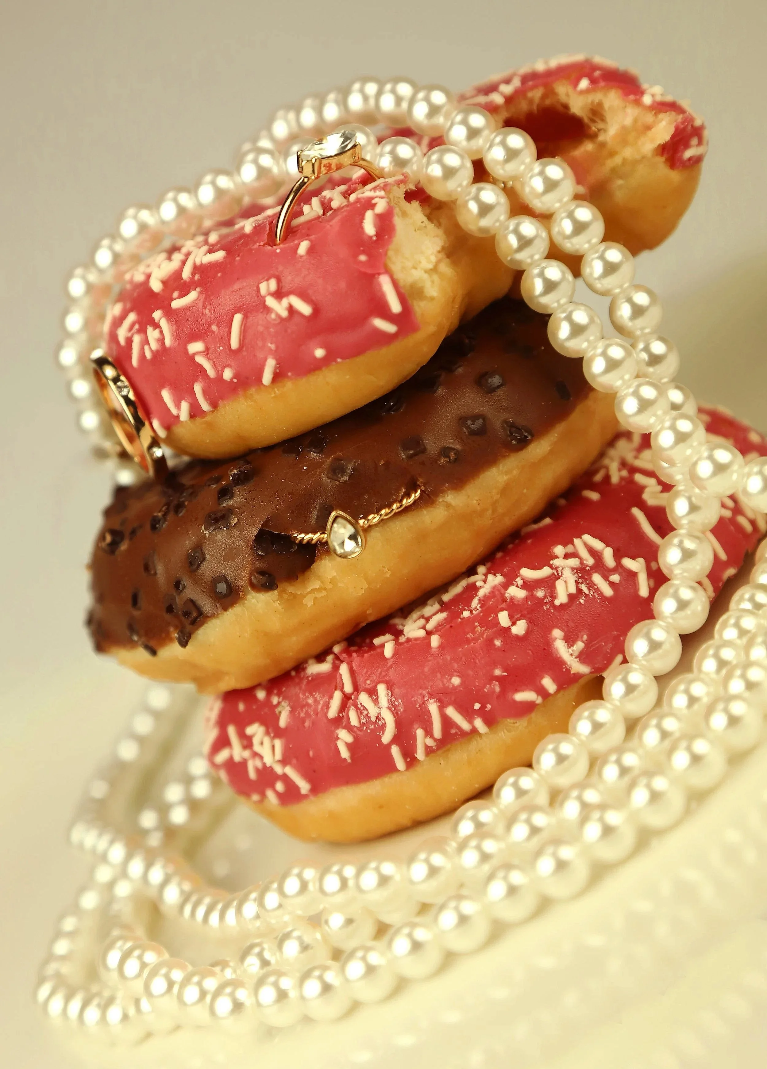 Stacked decorated donuts with pearl necklaces draped over them.