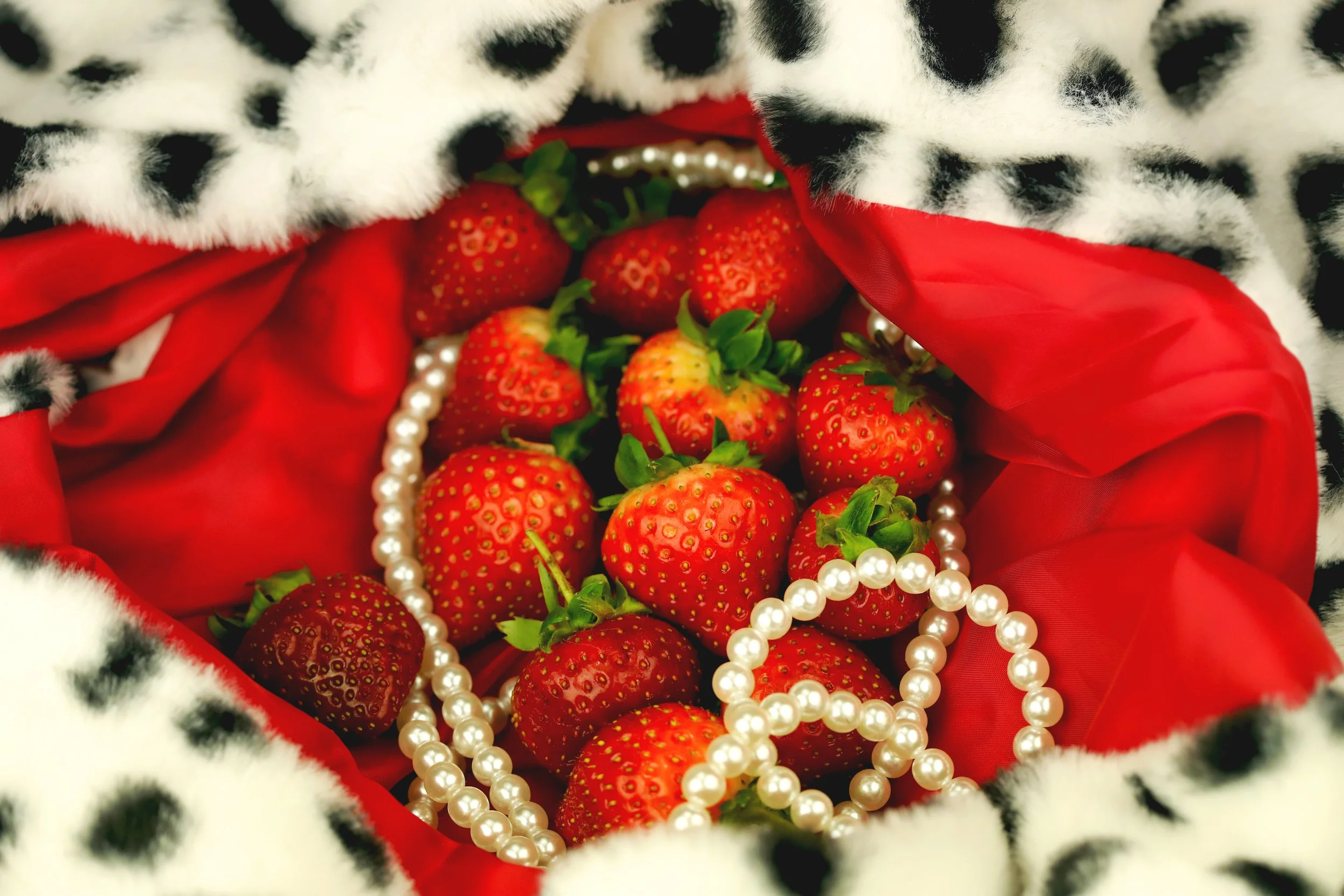 Fresh strawberries surrounded by a string of pearls inside a cloth with a red and black leopard print pattern.