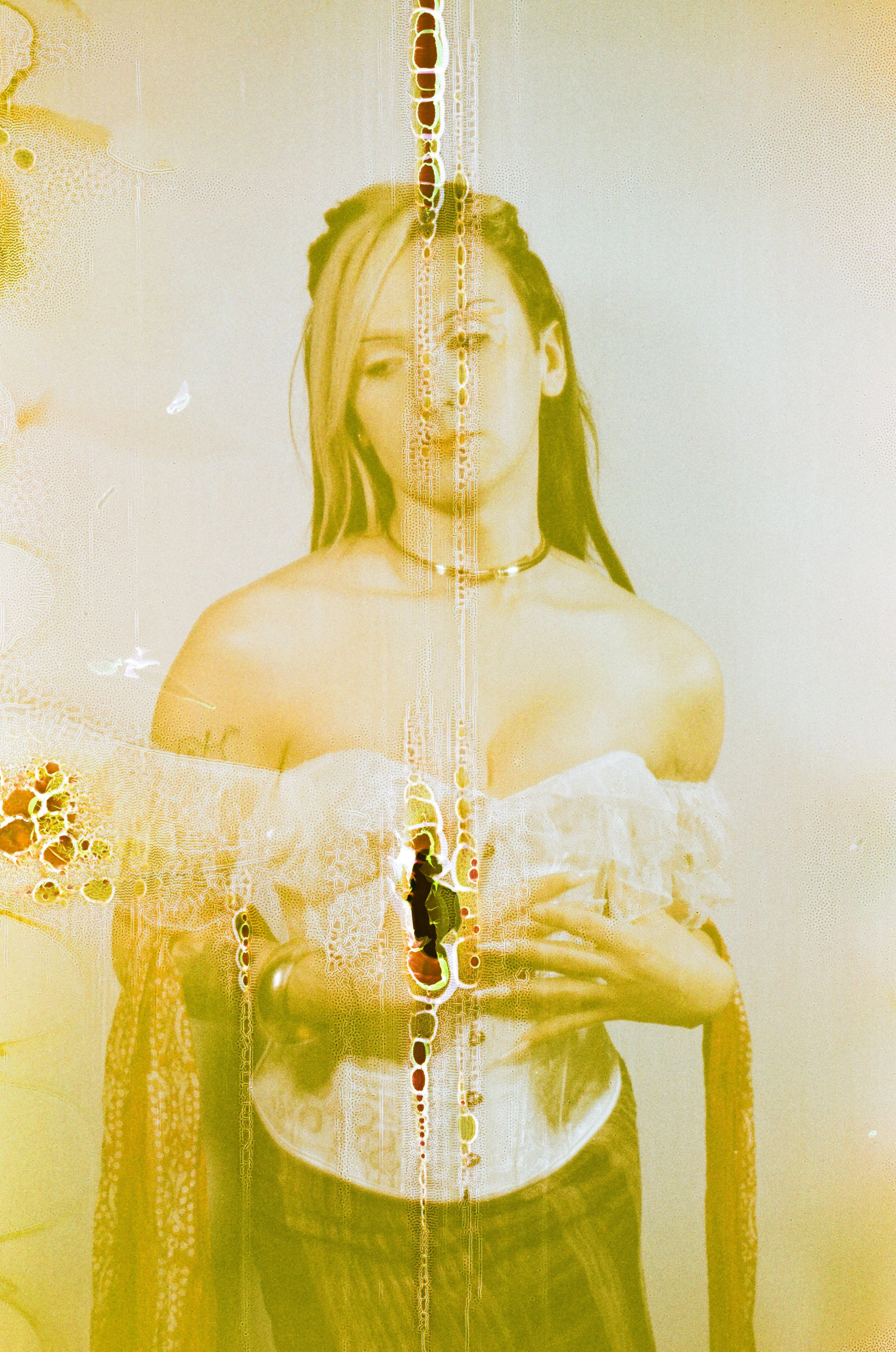 A woman with long hair, wearing an off-the-shoulder top and a choker, is standing behind a glass surface with yellow and orange streaks and patterns.