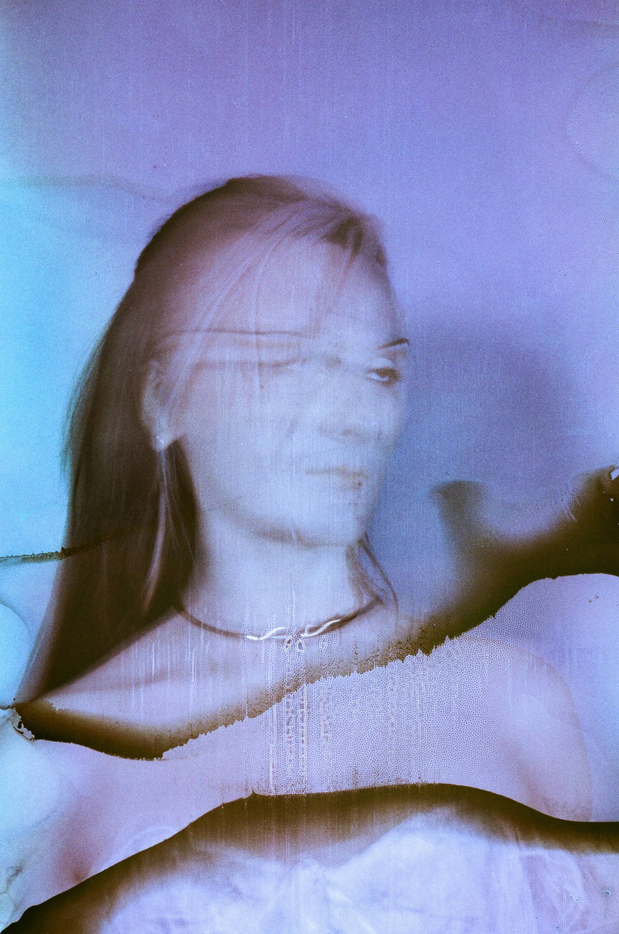 A woman with long hair, wearing a choker necklace and a zip-up top, smiling and looking to her right, with a purple background.