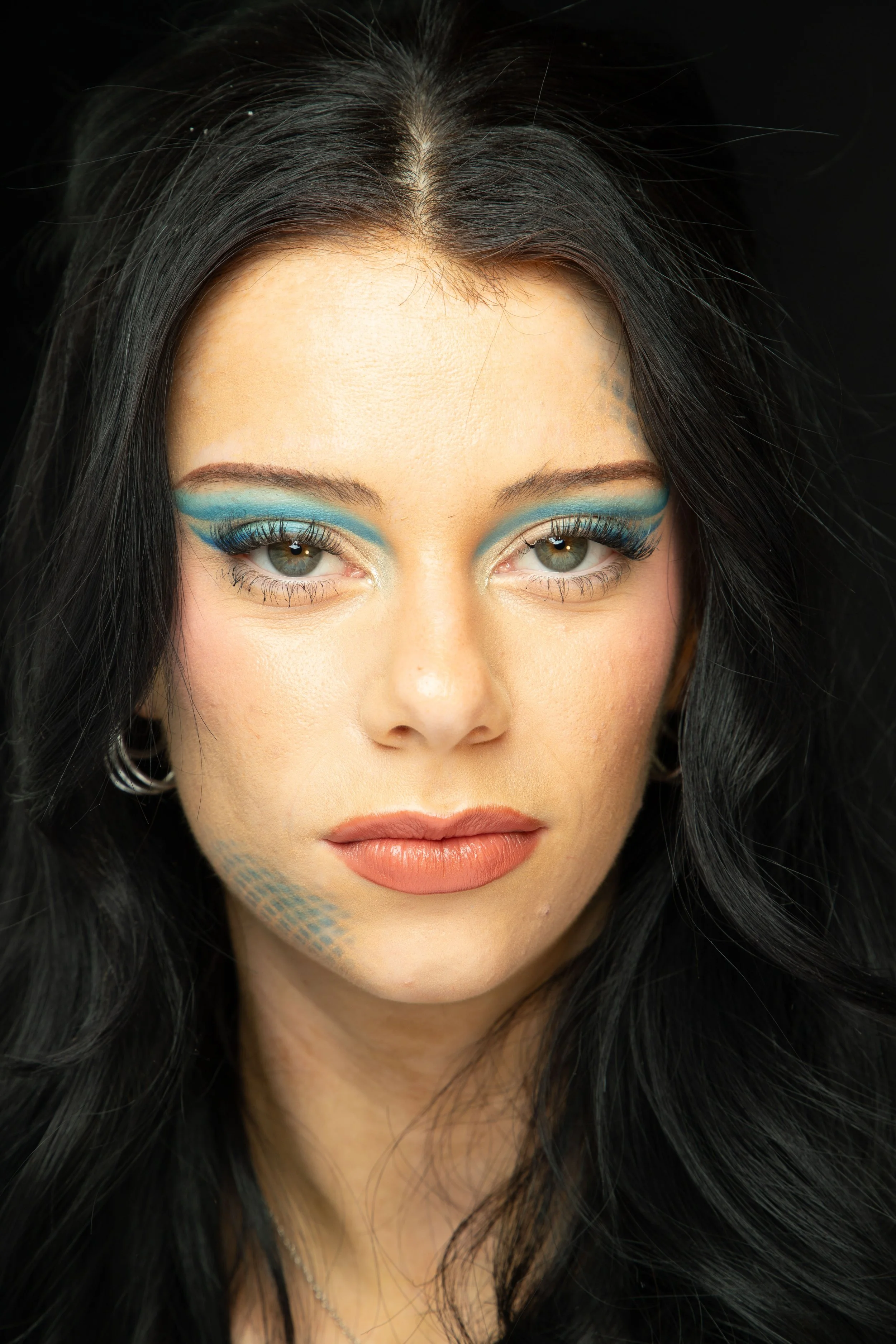A woman with long black hair, eye makeup with blue eyeshadow and eyeliner, and neutral lipstick.