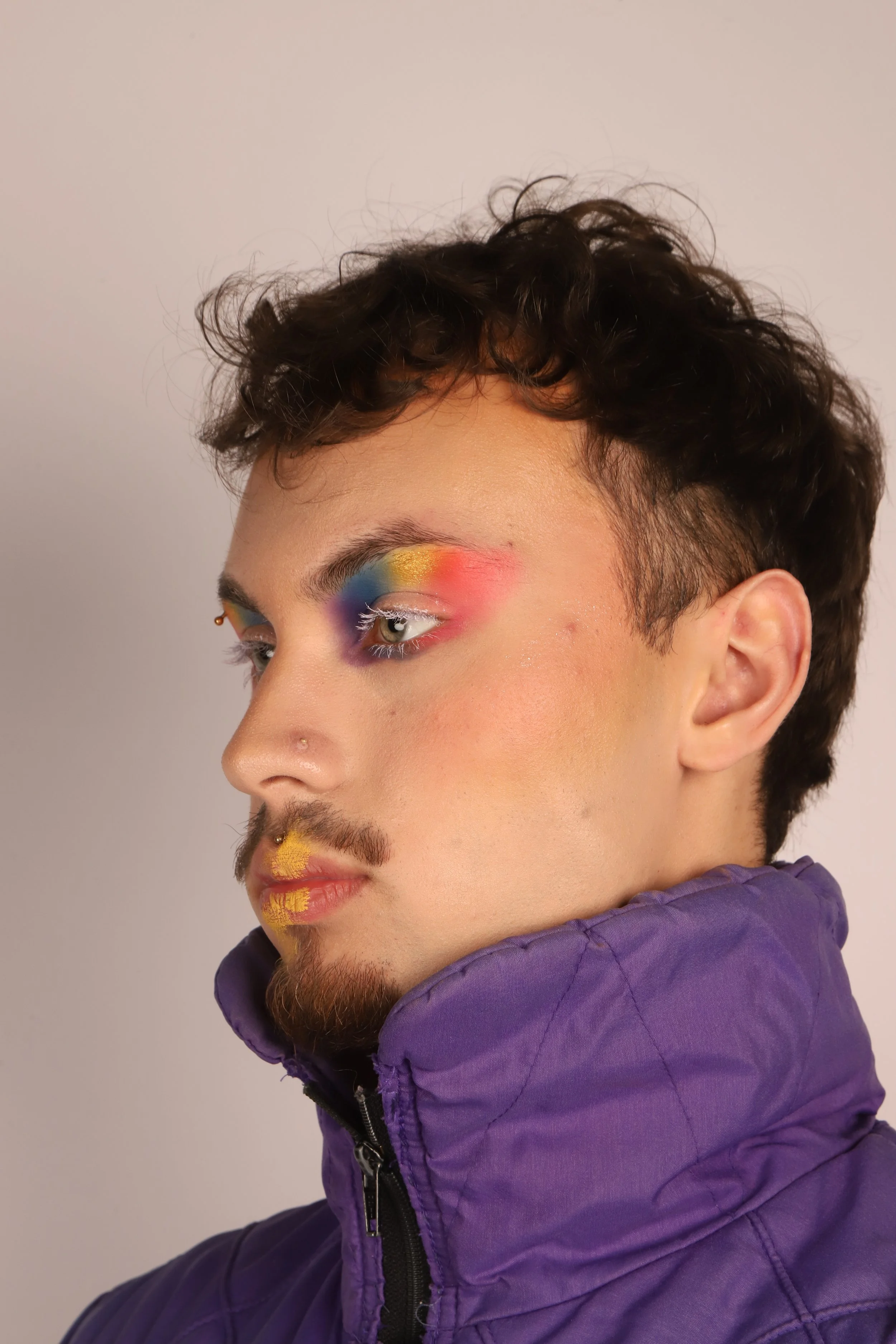 A person with colorful makeup, wearing a purple jacket, looking to the side.