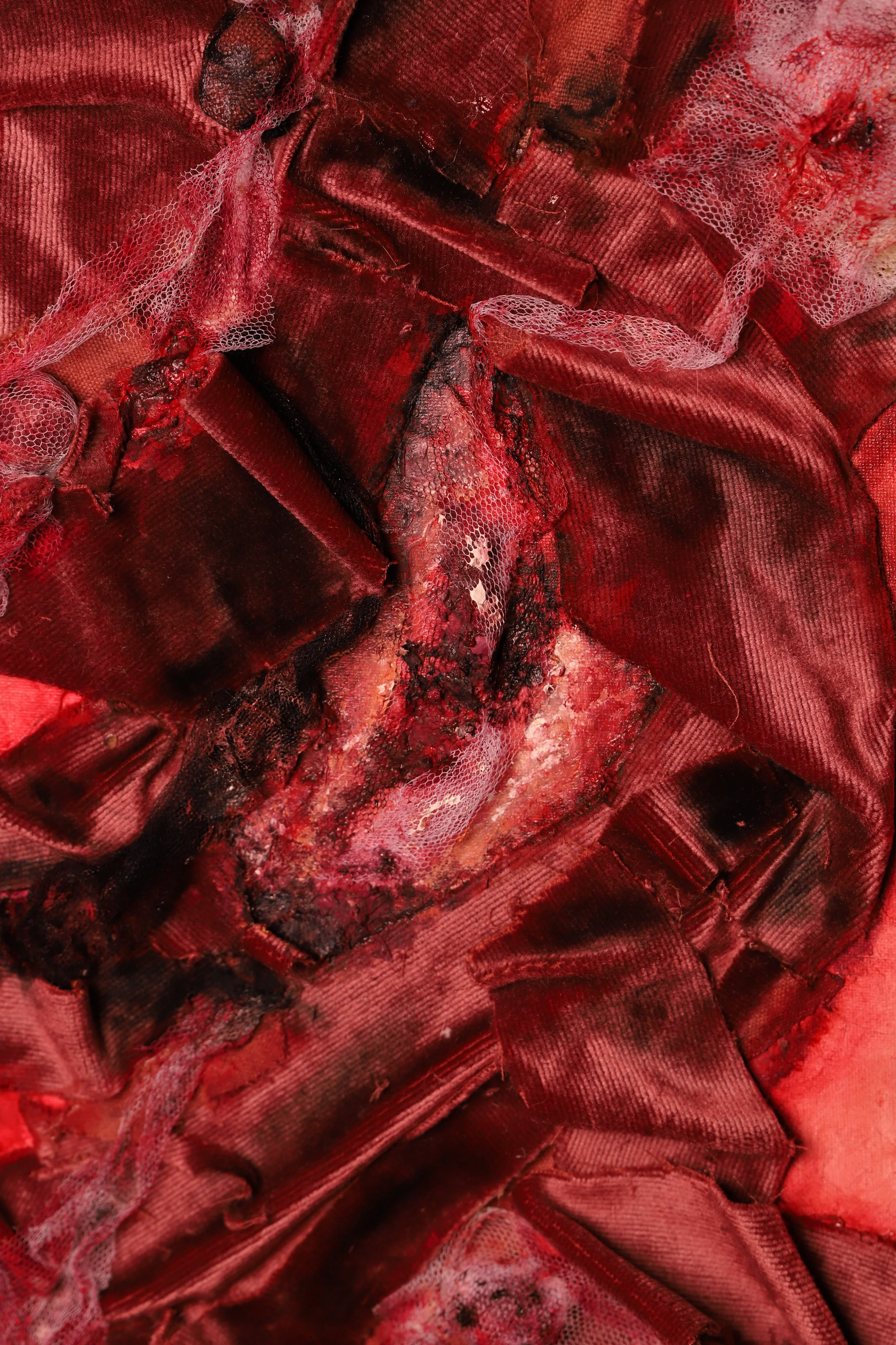 A close-up of a damaged, bloodstained piece of red fabric with tears and burns.