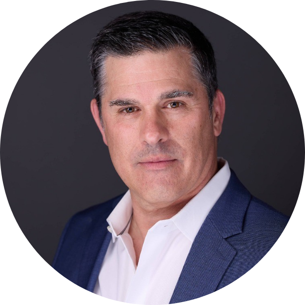 A middle-aged man with short dark hair, wearing a navy blue suit jacket and a white shirt, posing against a dark background.