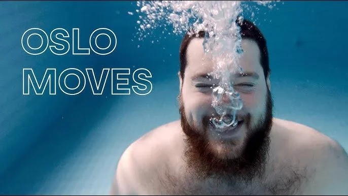 A man with a beard smiling underwater with bubbles around him. Text overlay says 'OSLO MOVES'.
