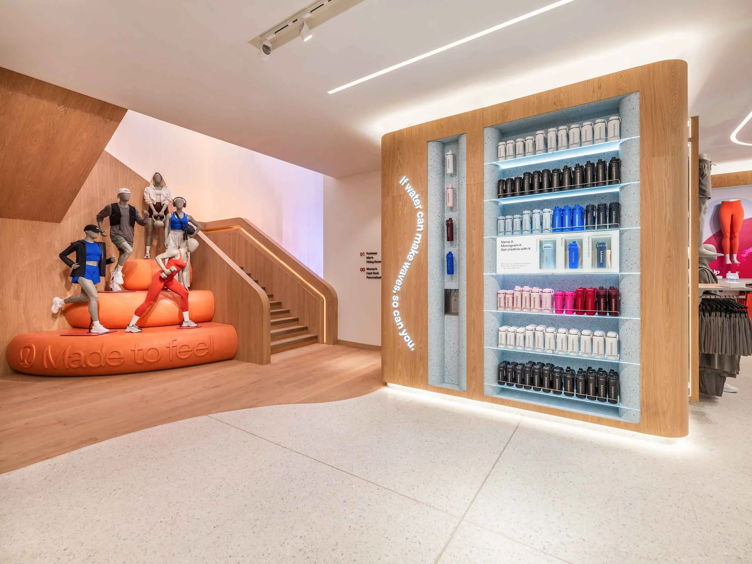 Mannequins with athletic clothing and accessories on wooden stairs inside a store. Shelves with water bottles and merchandise in the background.