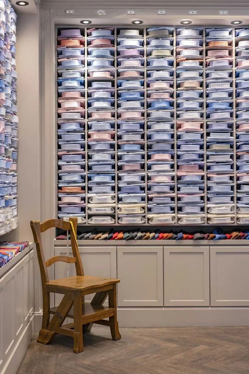 Wall of neatly folded pajamas or shirts in various pastel colors and patterns, with a wooden chair in front of the display in a clothing store.