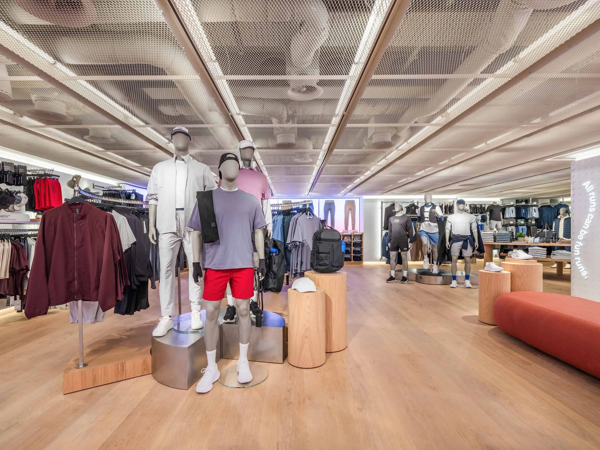 Mannequins dressed in sportswear and casual clothing displayed in a retail store with clothing racks and a seating area.