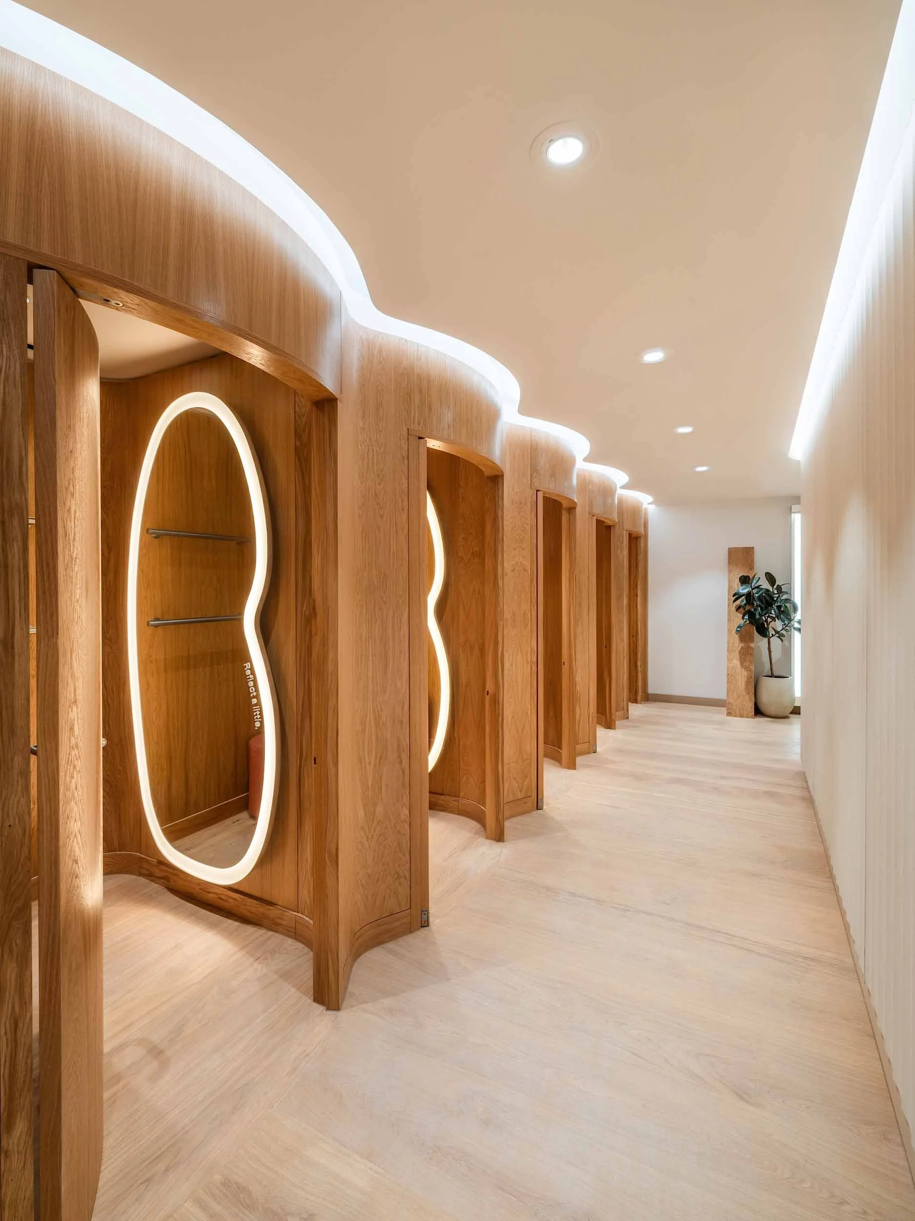 A hallway interior with wooden privacy booths, oval mirrors, and subtle LED lighting along the ceiling.