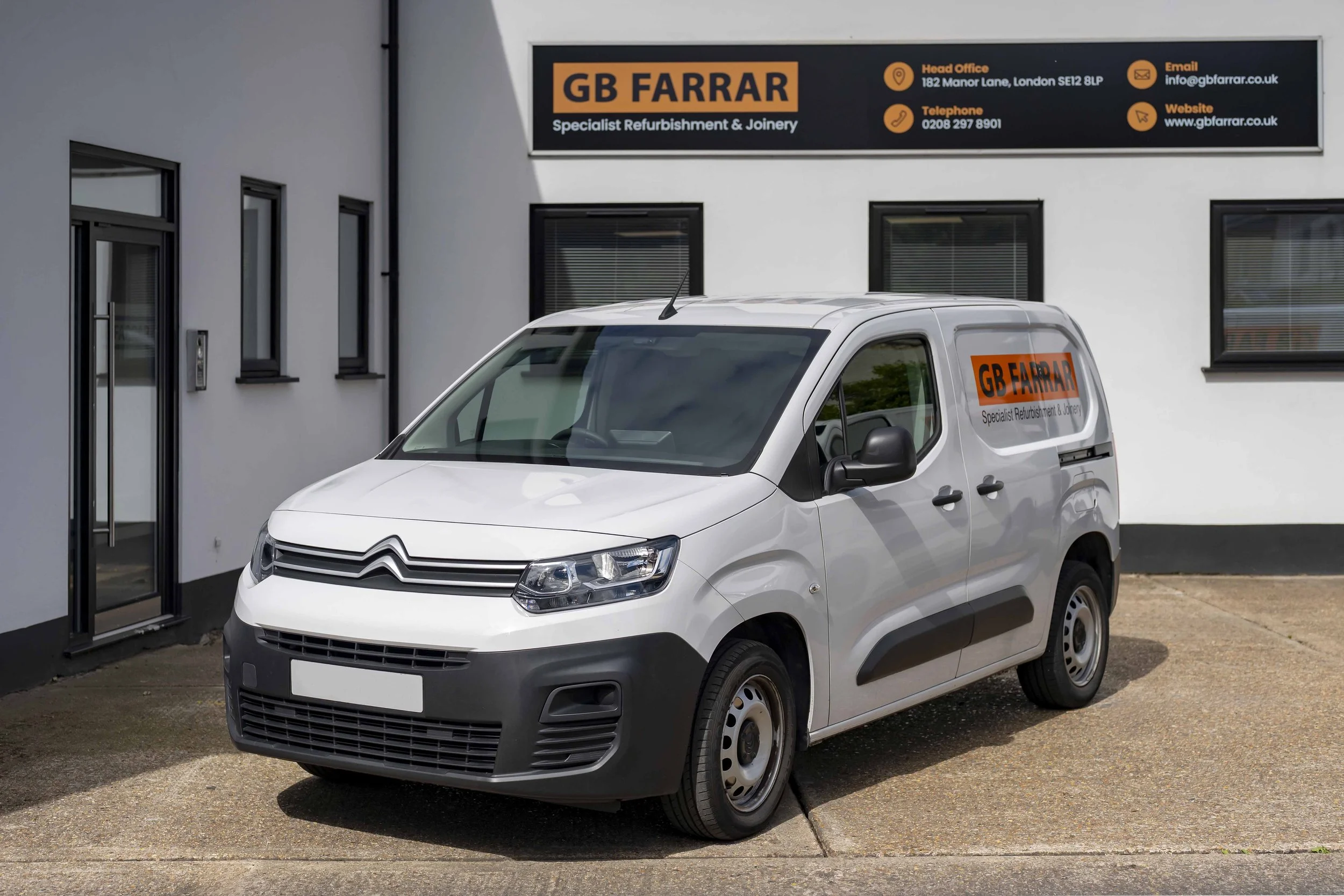 A white Citroën commercial van parked in front of a Manx white building with three windows and a sign for GB Farrar, a specialist refurbishment and joinery company. The sign displays contact information including address, email, telephone, and website.